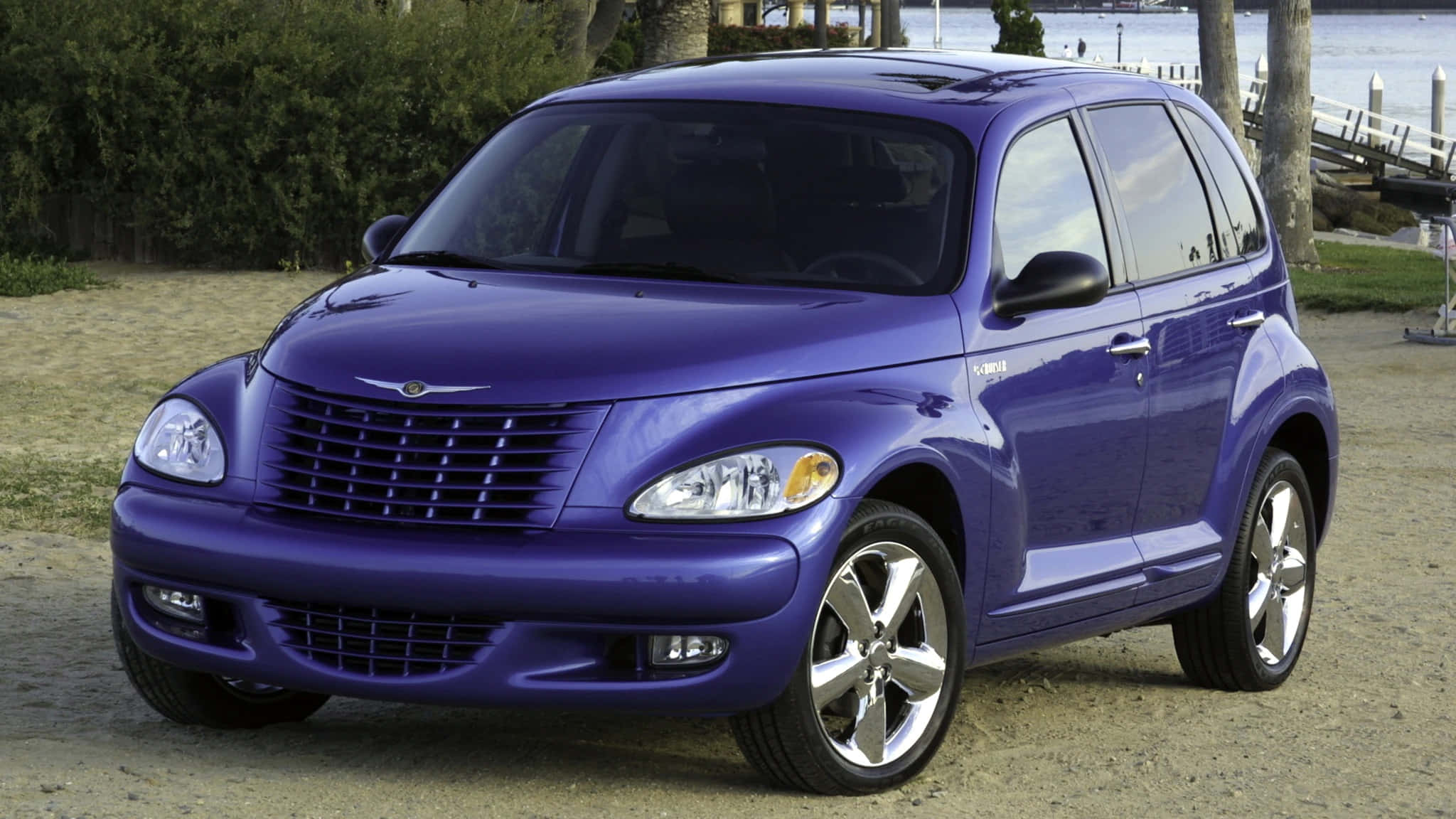 Chrysler Pt Cruiser 桌布 壁紙 — 一輛亮紫色嘅PT Cruiser停泊喺近水嘅碎石上，背景有樹木同碼頭。