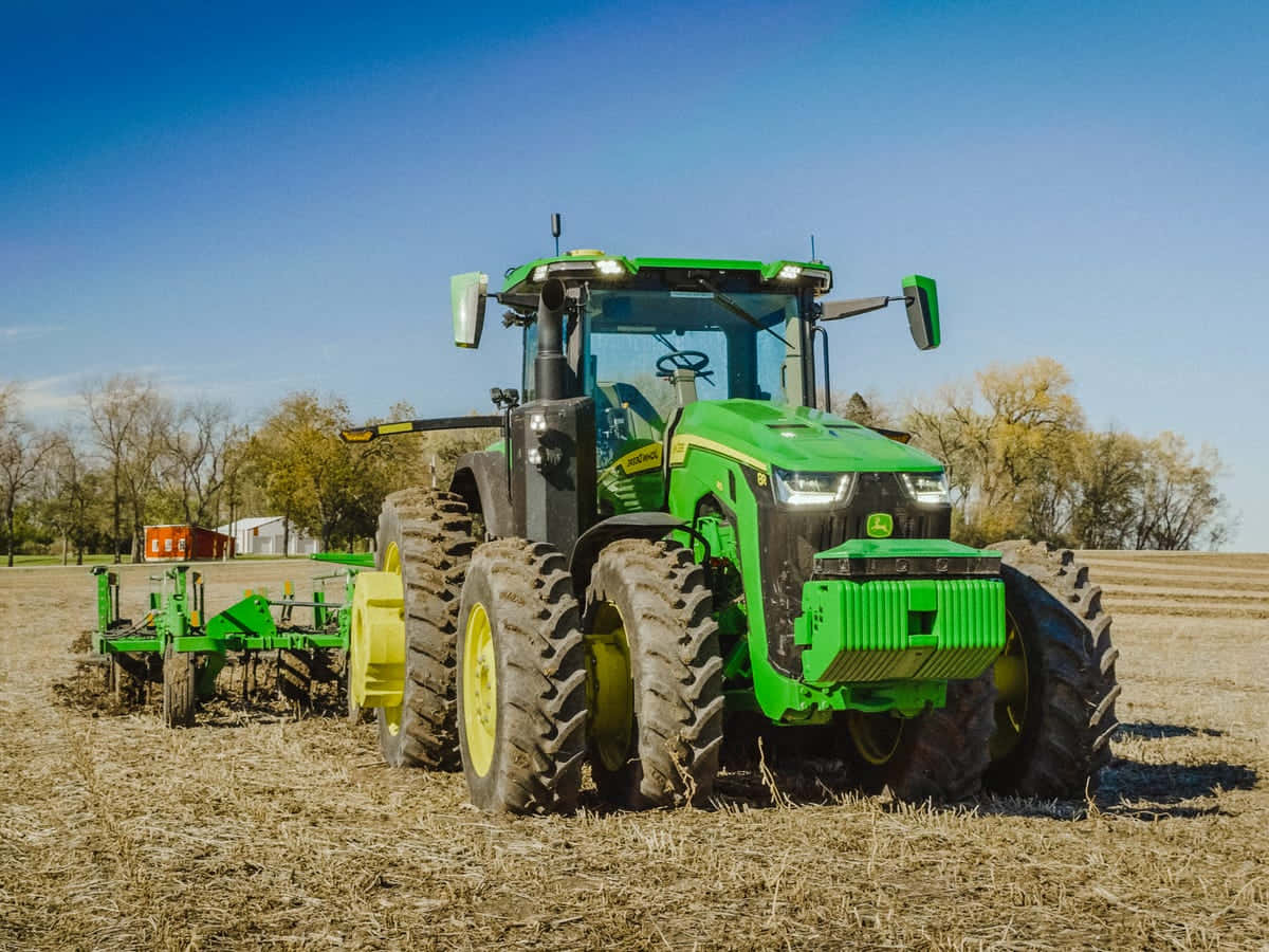 John Deere 桌布 壁紙 — 一輛亮綠色嘅John Deere拖拉機，黃色車輪，喺晴朗藍天下拖住犁穿過乾旱嘅收割田地。
