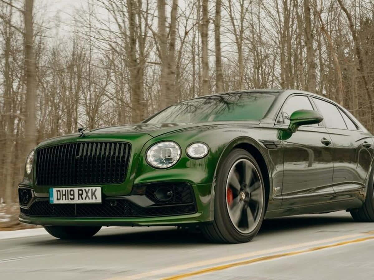 Bentley Flying Spur 桌布 壁紙 — 一輛亮綠色嘅賓利 Flying Spur 喺一條兩旁有光禿禿冬天樹木嘅森林道路上飛馳。