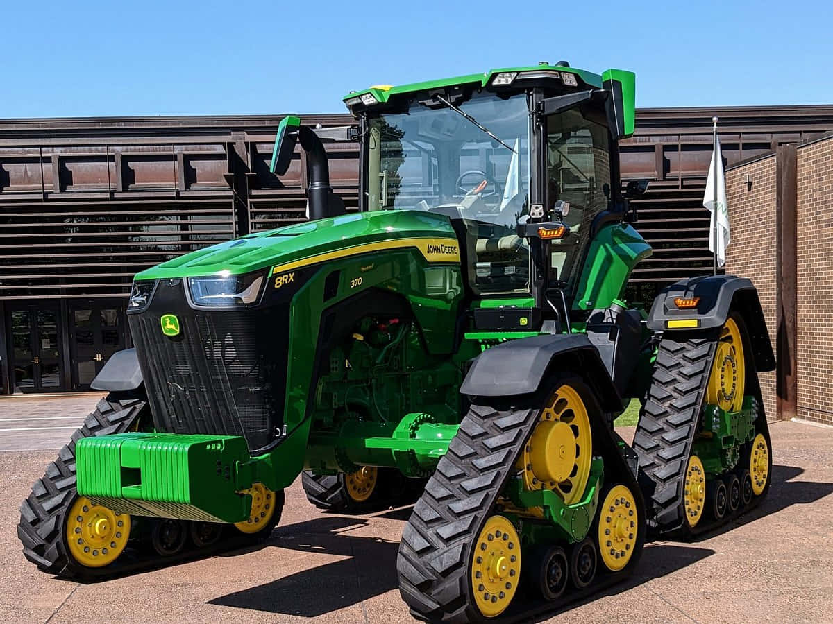 John Deere 桌布 壁紙 — 一輛亮綠色的約翰迪爾履帶拖拉機帶有黃色車輪，停在鋪砌的路面上，天空湛藍清澈。