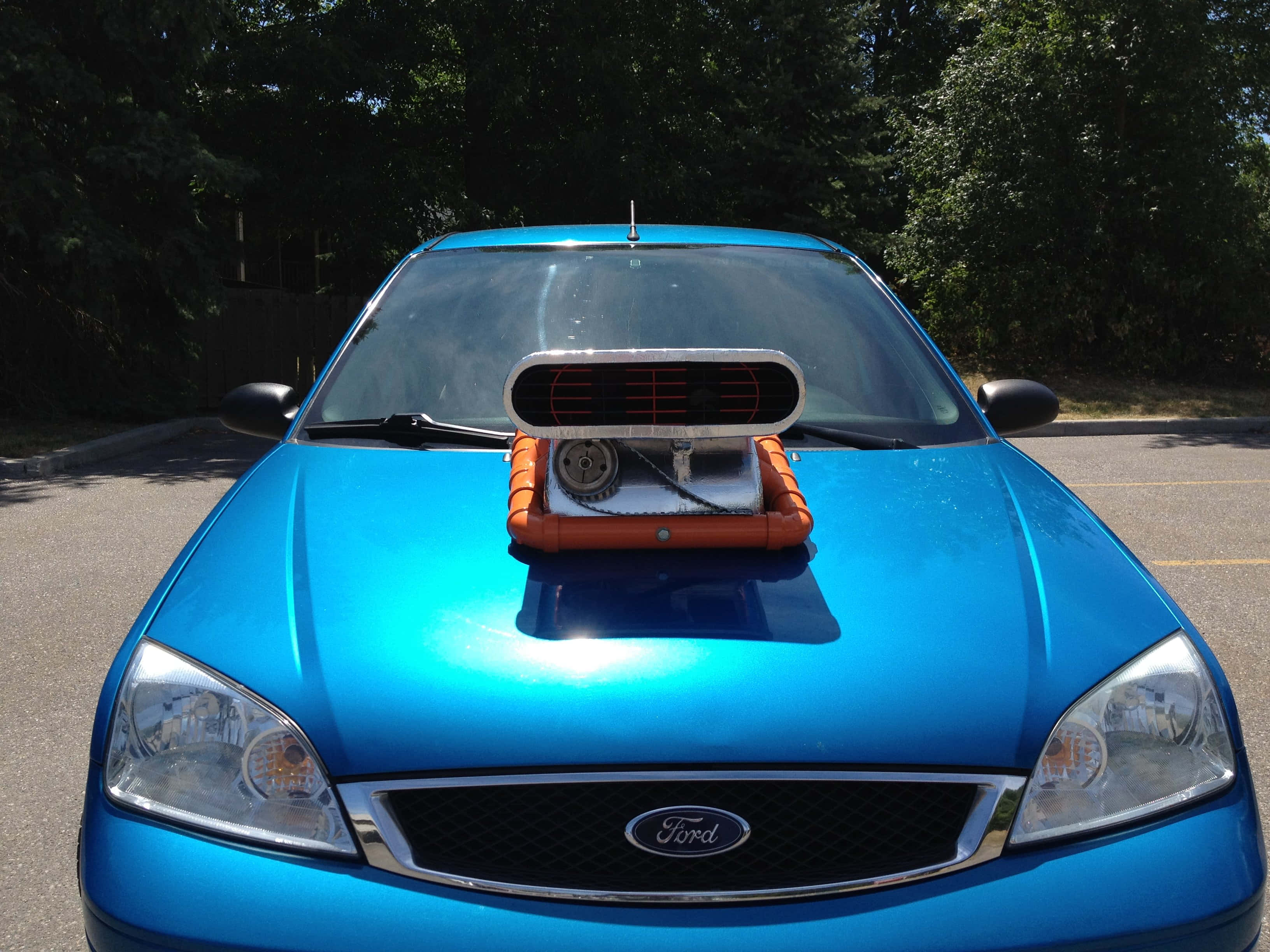 Car Hood 桌布 壁紙 — 一輛亮藍色福特汽車，配有定制引擎蓋進氣口和橙色點綴，停在陽光明媚、樹木環繞的停車場。
