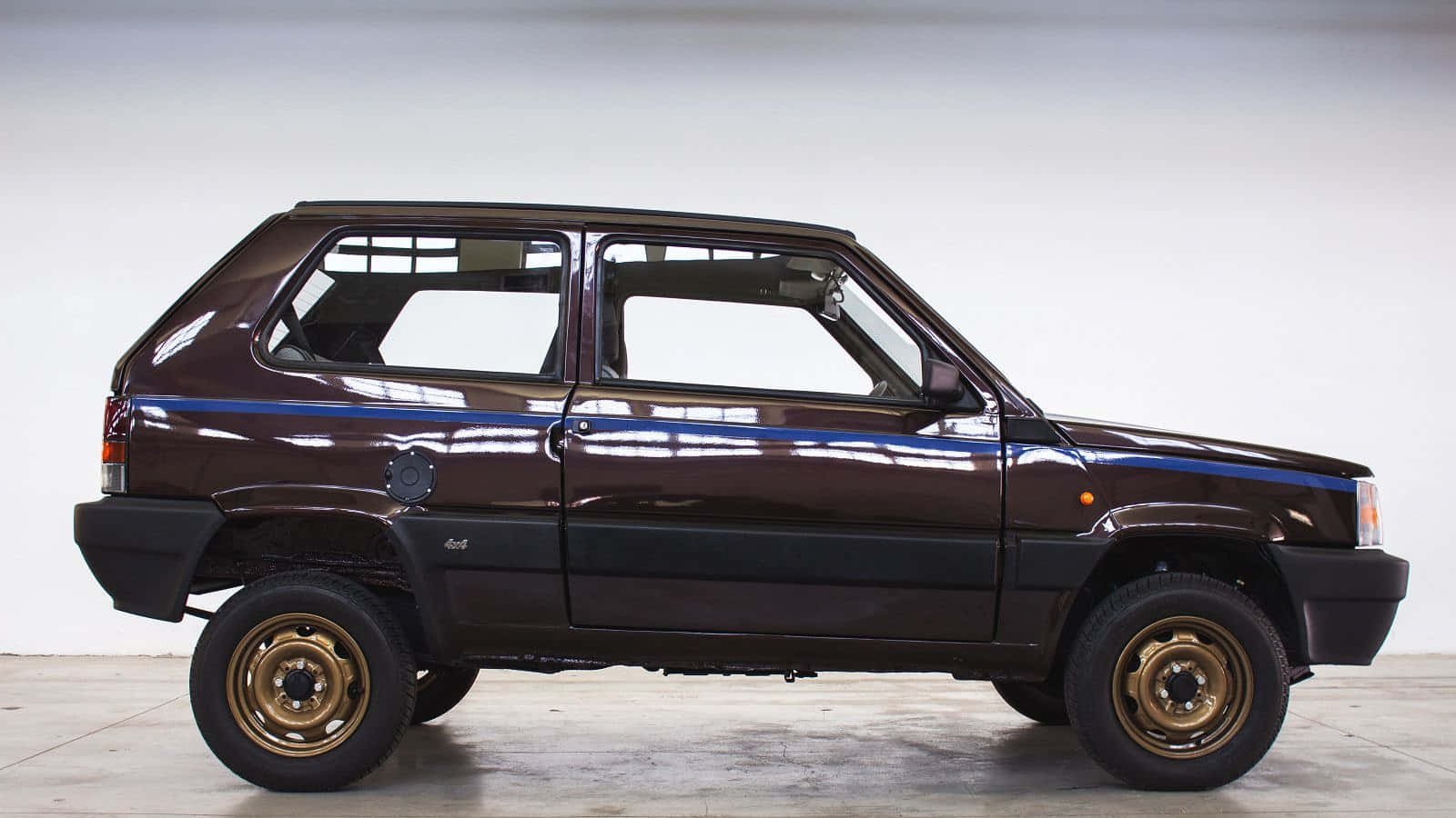 Fiat Panda 桌布 壁紙 — 一輛亮面棕色Fiat Panda 4x4，配金色輪圈和藍色條紋，停在明亮的攝影棚空間中。