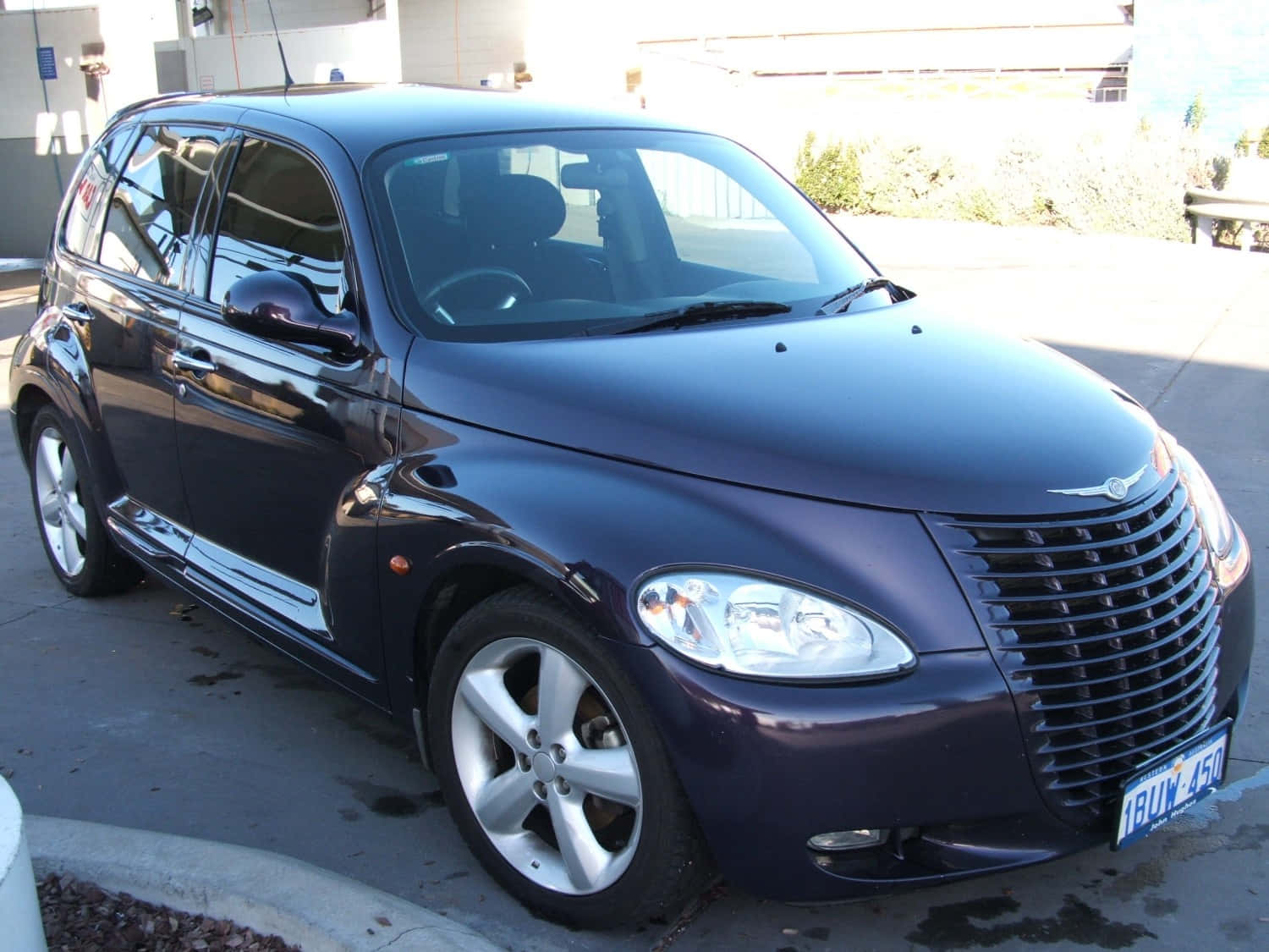Chrysler Pt Cruiser 桌布 壁紙 — 一輛亮面深紫色PT Cruiser停放在陽光明媚的混凝土停車場上，車身曲線反射光線。