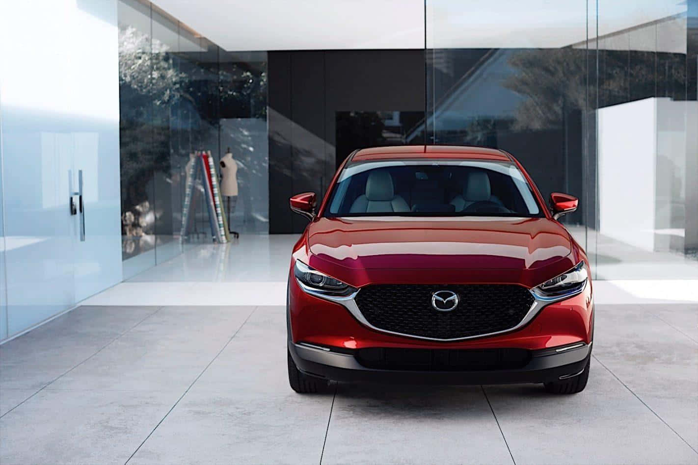 Mazda Cx-30 桌布 壁紙 — 一輛亮面紅色Mazda SUV在時尚現代玻璃牆展廳中正面朝前，地板具有反射效果。