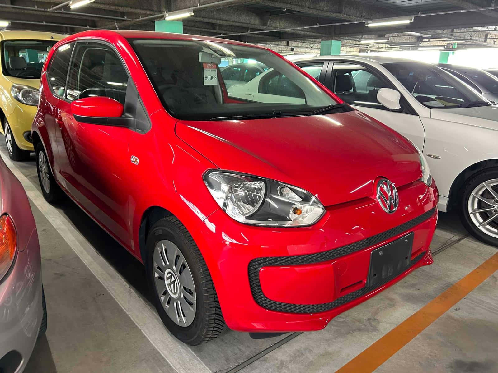  壁紙 — 一輛亮面紅色Volkswagen up!停泊在光線充足的室內停車場，附近有其他車輛。