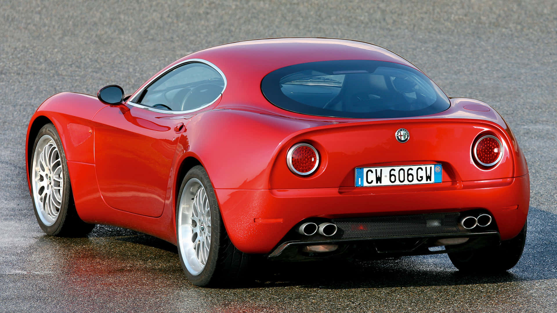 Alfa Romeo 8c Competizione 桌布 壁紙 — 一輛亮面紅色愛快羅密歐跑車停在濕瀝青上，配備銀色輪圈和雙排氣管。