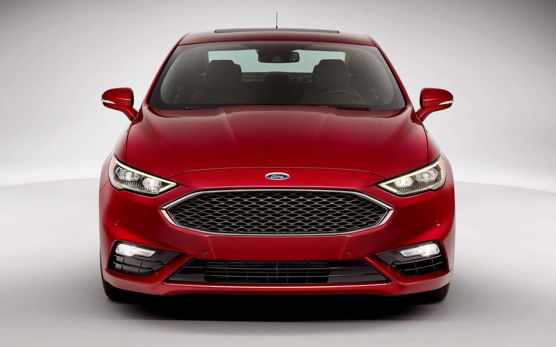 Ford Fusion 桌布 壁紙 — 一輛亮面紅色福特房車在極簡風格的工作室中正面朝前，柔和燈光突顯其流線型現代設計。