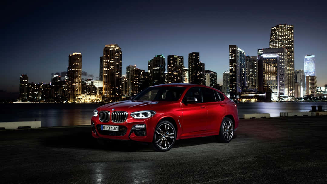 Bmw X4 桌布 壁紙 — 一輛亮麗的紅色BMW X4 SUV在黃昏時停泊，背後的水面反射出閃爍的城市天際線。