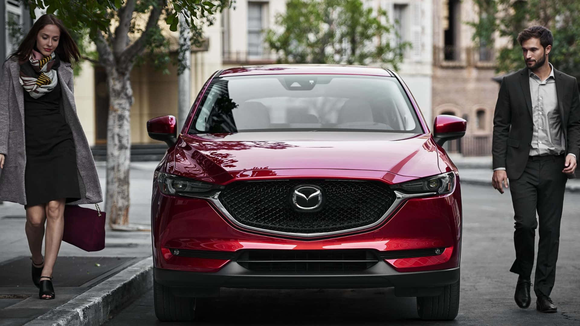 Mazda Cx-5 桌布 壁紙 — 一輛亮麗的紅色Mazda CX-5在城市的街道上向前，兩旁有兩位行人走過。