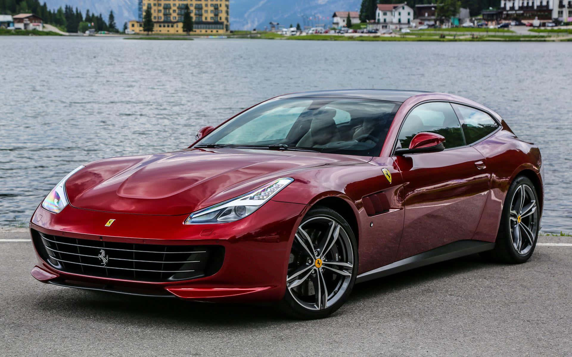 Ferrari Gtc4lusso 桌布 壁紙 — 一輛亮麗的紅色法拉利 GTC4Lusso 停泊在寧靜的湖邊，背景有山脈和建築物。
