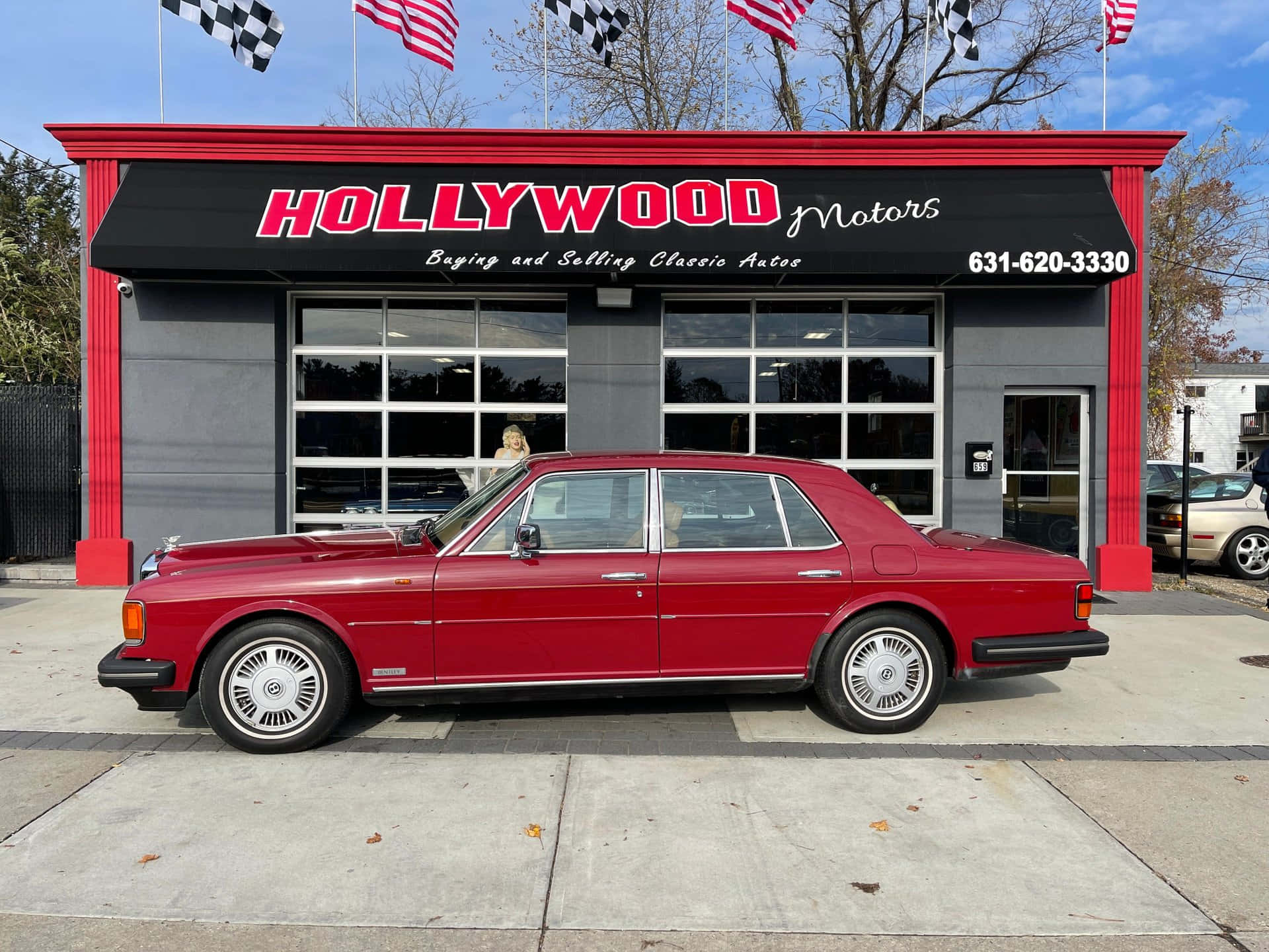 Bentley Eight 桌布 壁紙 — 一輛亮麗的紅色經典汽車停在紅黑相間的Hollywood Motors經銷店前，背景是晴朗的藍天。