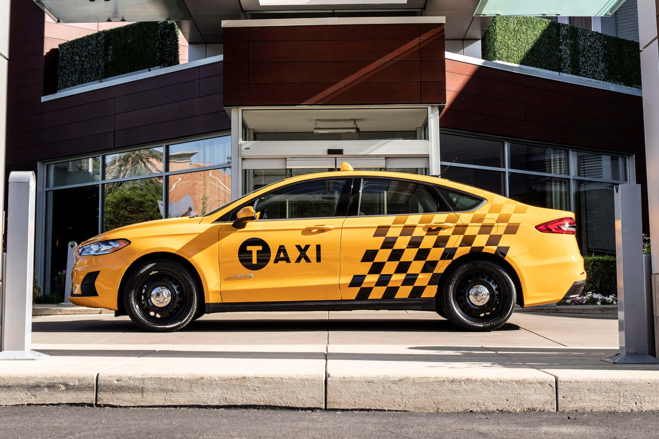taxi 桌布 壁紙 — 一輛亮黃色帶黑色棋盤格圖案的的士在陽光明媚的日子停在一棟現代建築外。