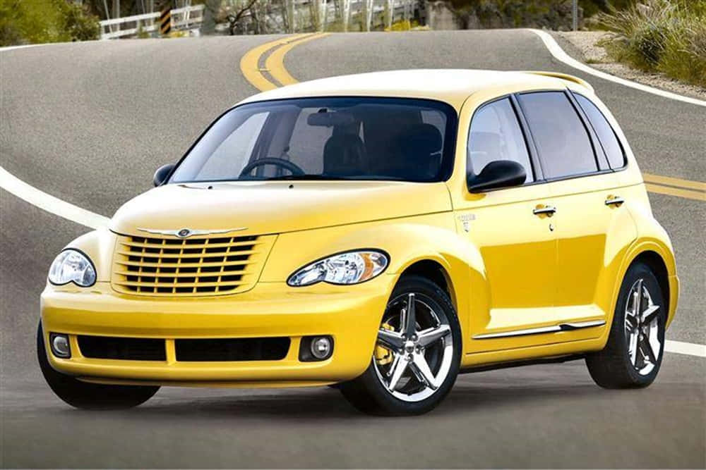 Chrysler Pt Cruiser 桌布 壁紙 — 一輛亮黃色的PT Cruiser在晴朗的白天沿著一條雙黃線的蜿蜒瀝青道路行駛。