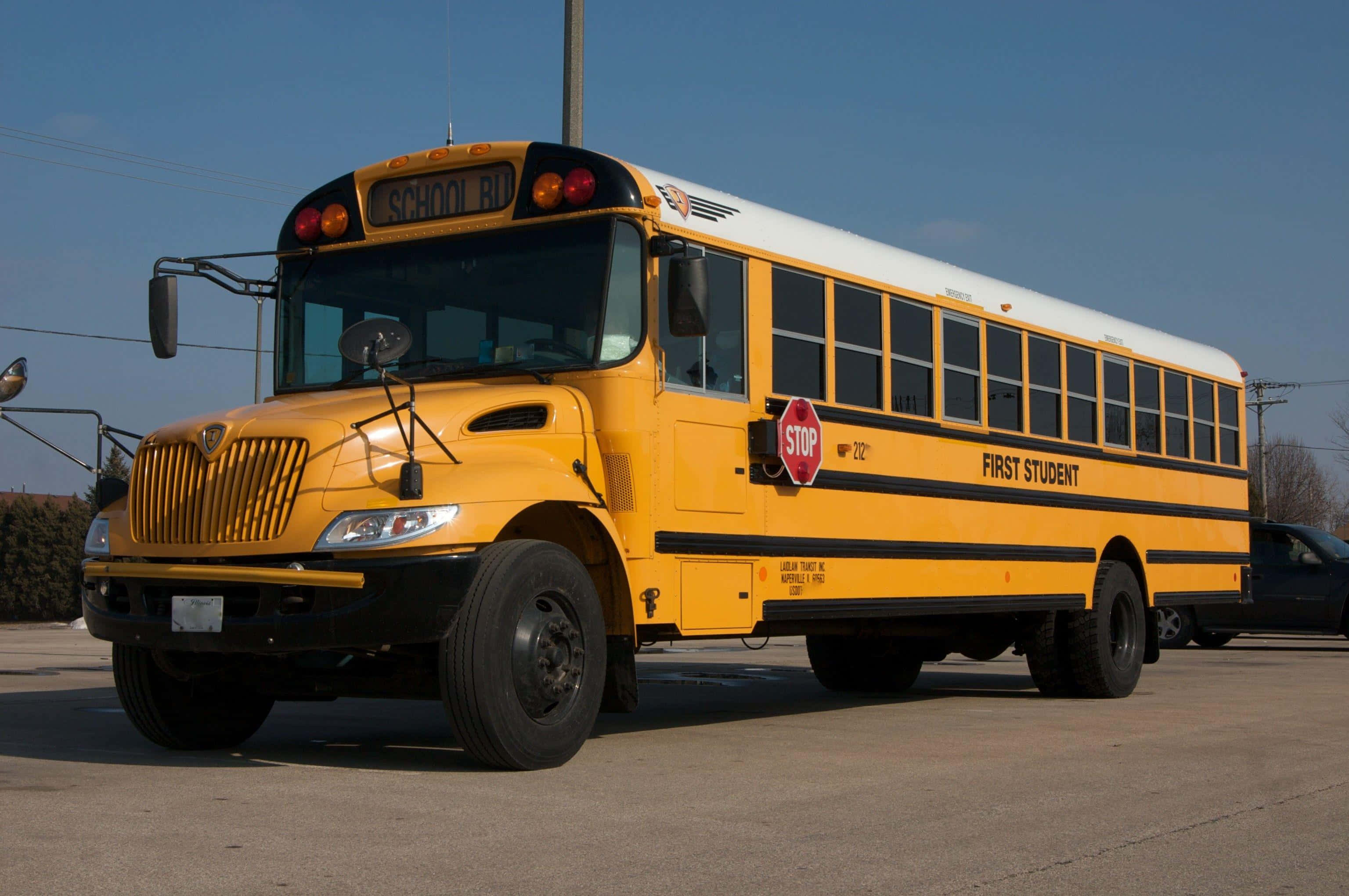 Yellow School Bus 桌布 壁紙 — 一輛亮黃色的校車，帶有「FIRST STUDENT」品牌標誌，在晴朗的日子停放在清澈的藍天下。