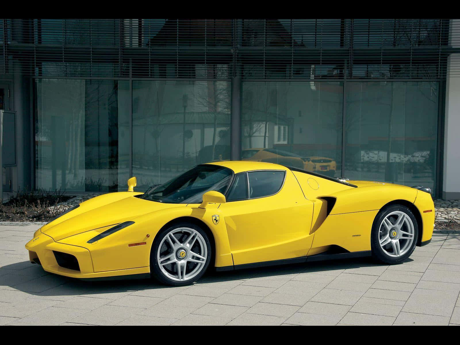 Ferrari Enzo 桌布 壁紙 — 一輛亮黃色的法拉利Enzo跑車停泊在現代玻璃建築前的瓷磚廣場上。