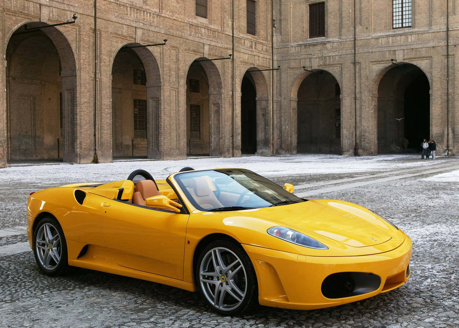 Ferrari F430 桌布 壁紙 — 一輛亮黃色的法拉利Spider停泊在鵝卵石庭院前，面對一座宏偉的石拱廊建築。