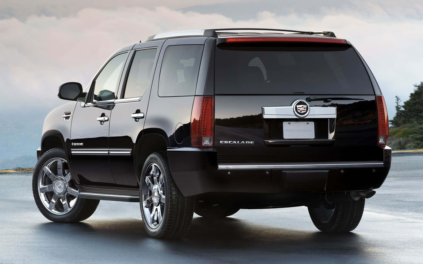 Cadillac Escalade 桌布 壁紙 — 一輛亮黑色Cadillac Escalade SUV停在濕漉漉的路面上，背景是陰天和遠處的樹木。