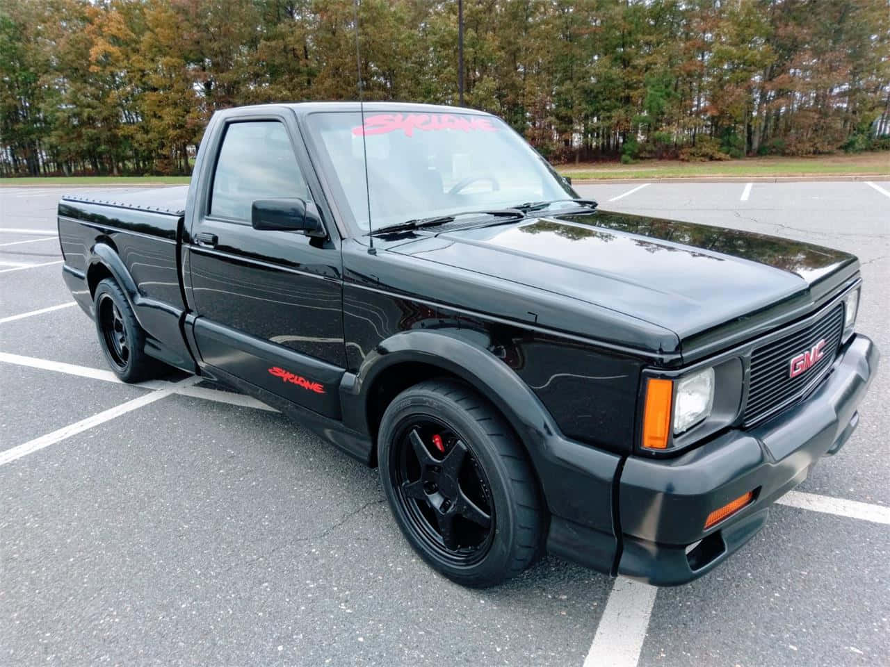Gmc Syclone 桌布 壁紙 — 一輛亮黑色GMC Syclone皮卡車，帶有紅色點綴，停在秋天的停車場。