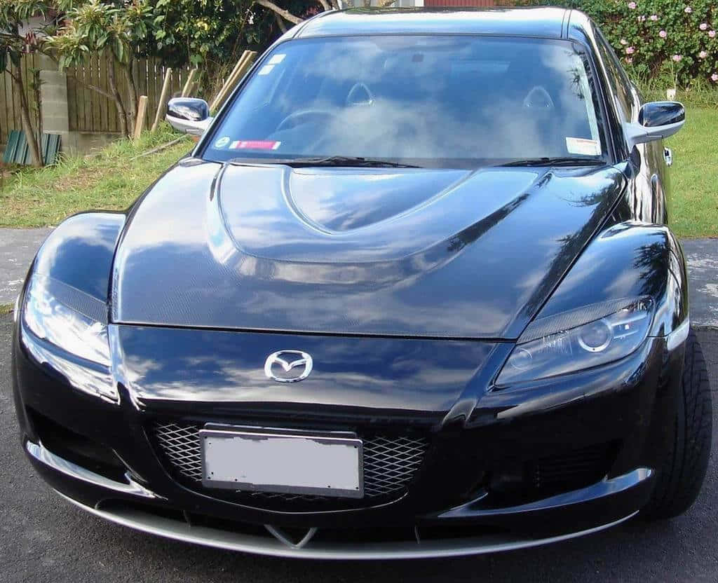 Car Hood 桌布 壁紙 — 一輛亮黑色Mazda RX-8跑車停在瀝青路上，背景有綠化和木柵欄。