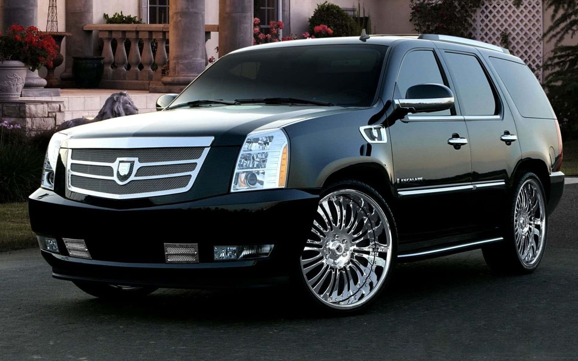 Cadillac Xlr 桌布 壁紙 — 一輛亮黑色凱迪拉克 Escalade 配備定制鍍鉻輪圈，停在有紅花的石頭豪宅前。