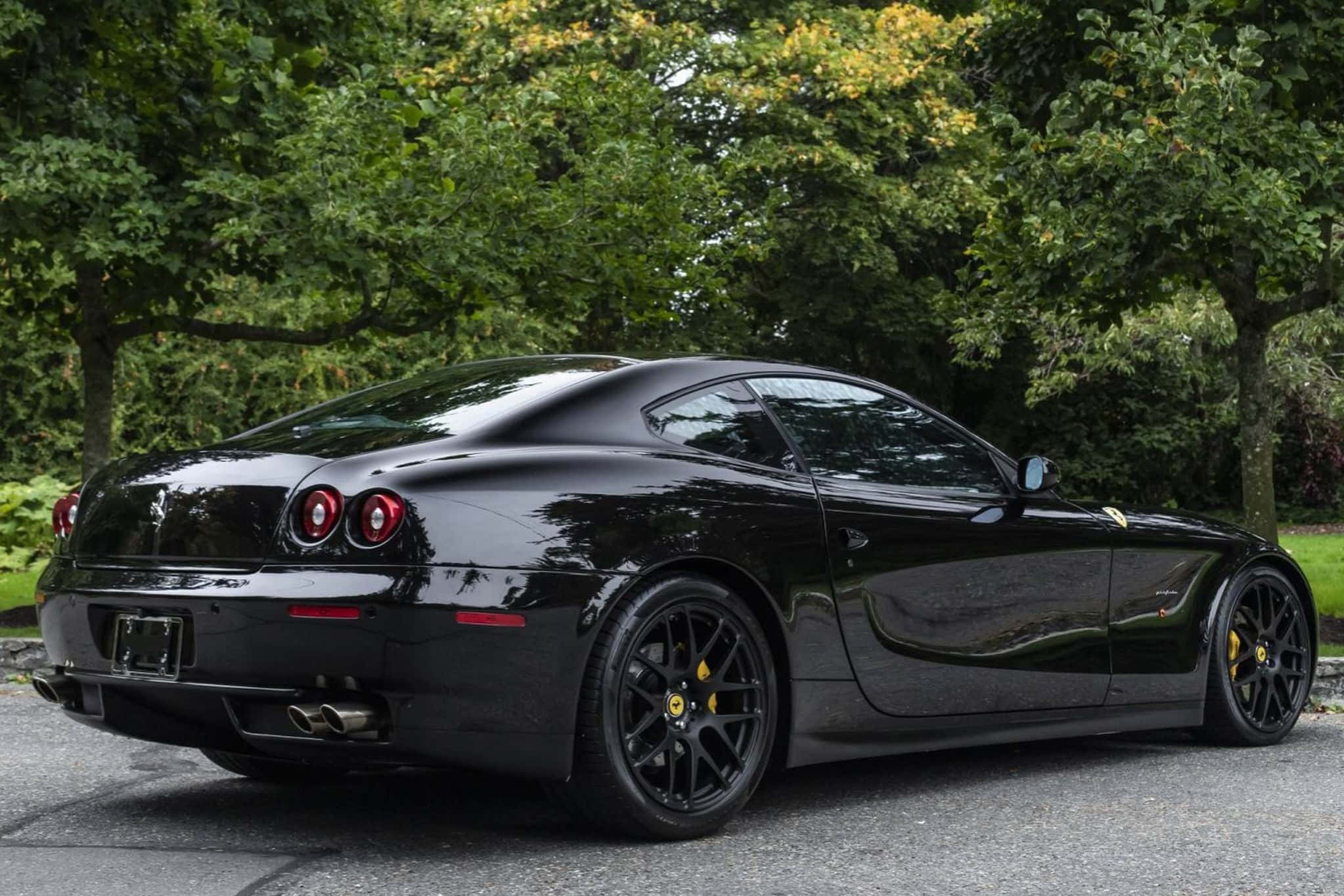 Ferrari 612 Scaglietti 桌布 壁紙 — 一輛亮黑色法拉利612 Superamerica停在瀝青路上，背景是茂密的綠樹。