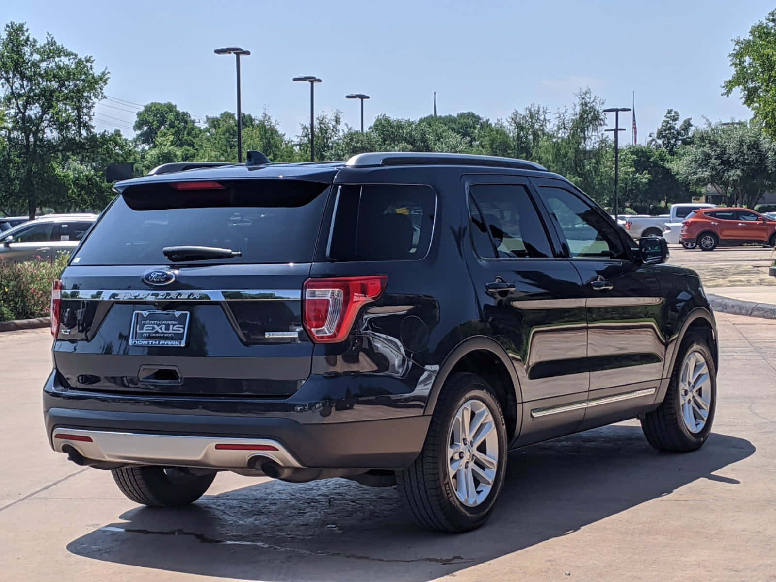 Ford Explorer 桌布 壁紙 — 一輛亮黑色福特Explorer SUV停泊在陽光明媚的經銷商場地上，背景有樹木和其他汽車。