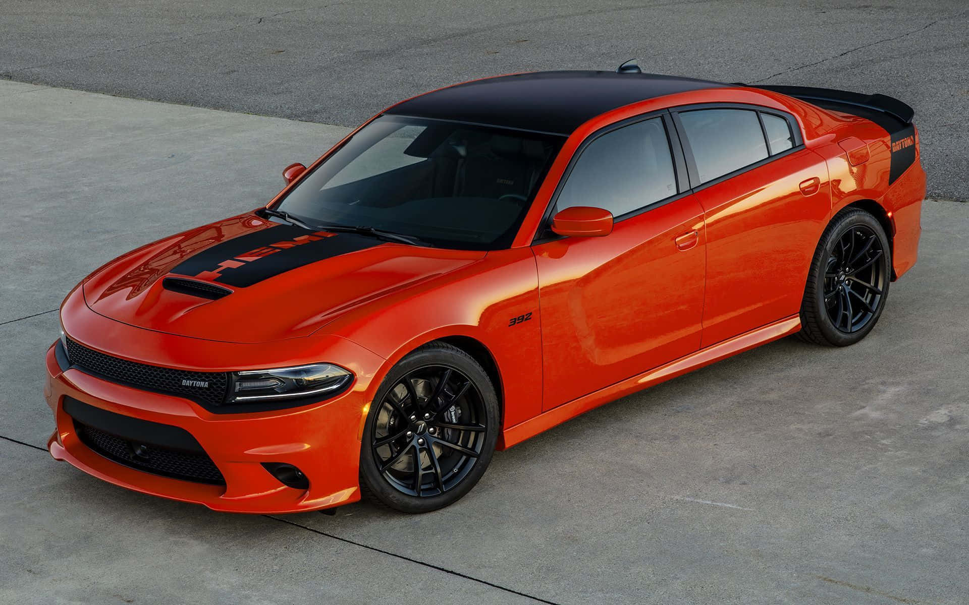 Dodge Charger 桌布 壁紙 — 一輛充滿活力的橙色 Dodge Charger Hellcat，帶有黑色飾邊和輪胎，停在混凝土表面上。