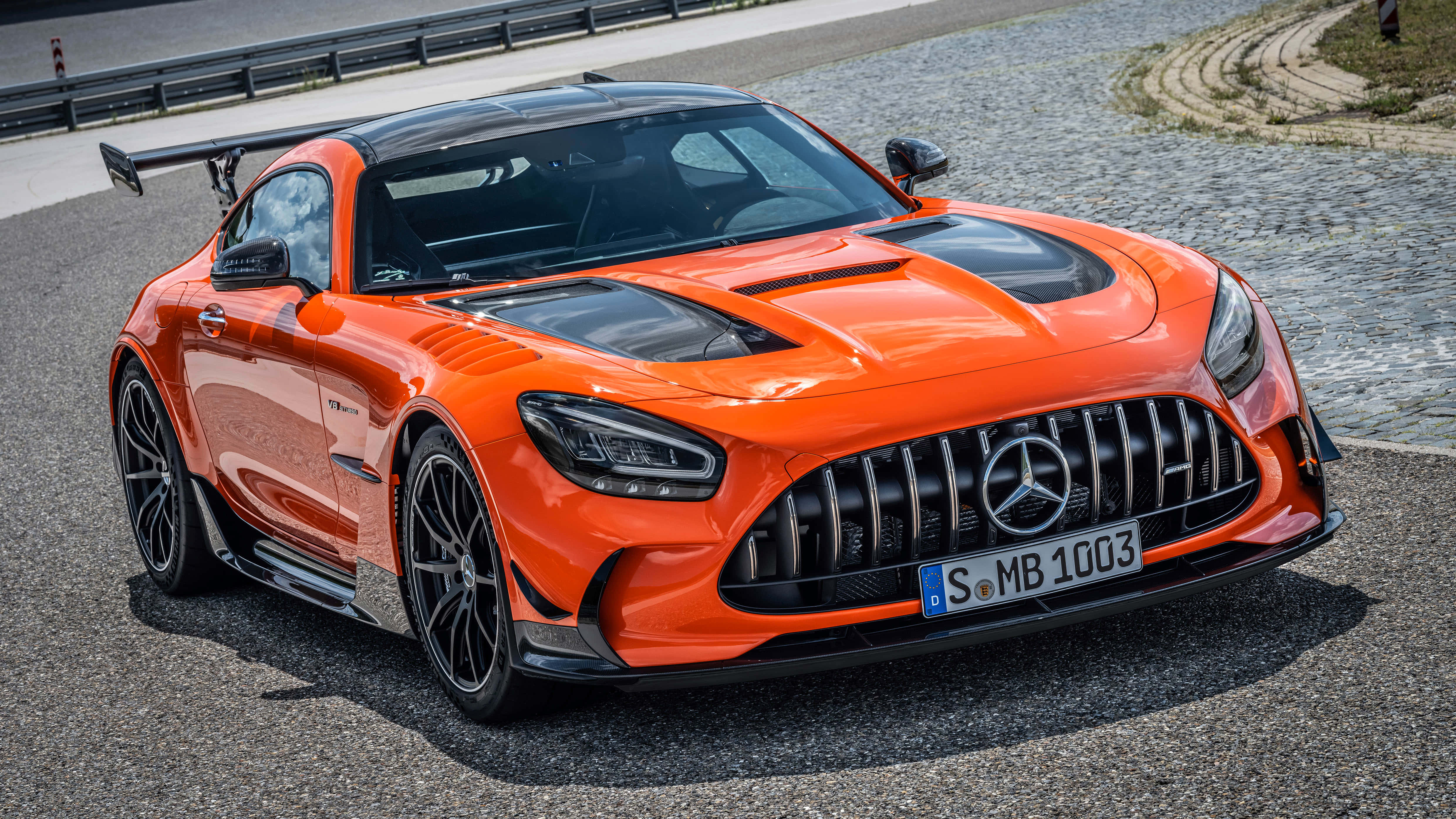 Black And Orange 桌布 壁紙 — 一輛充滿活力的橙色 Mercedes-AMG GT R 賽車，帶有黑色飾邊，停在明亮的日光下的鵝卵石路上。
