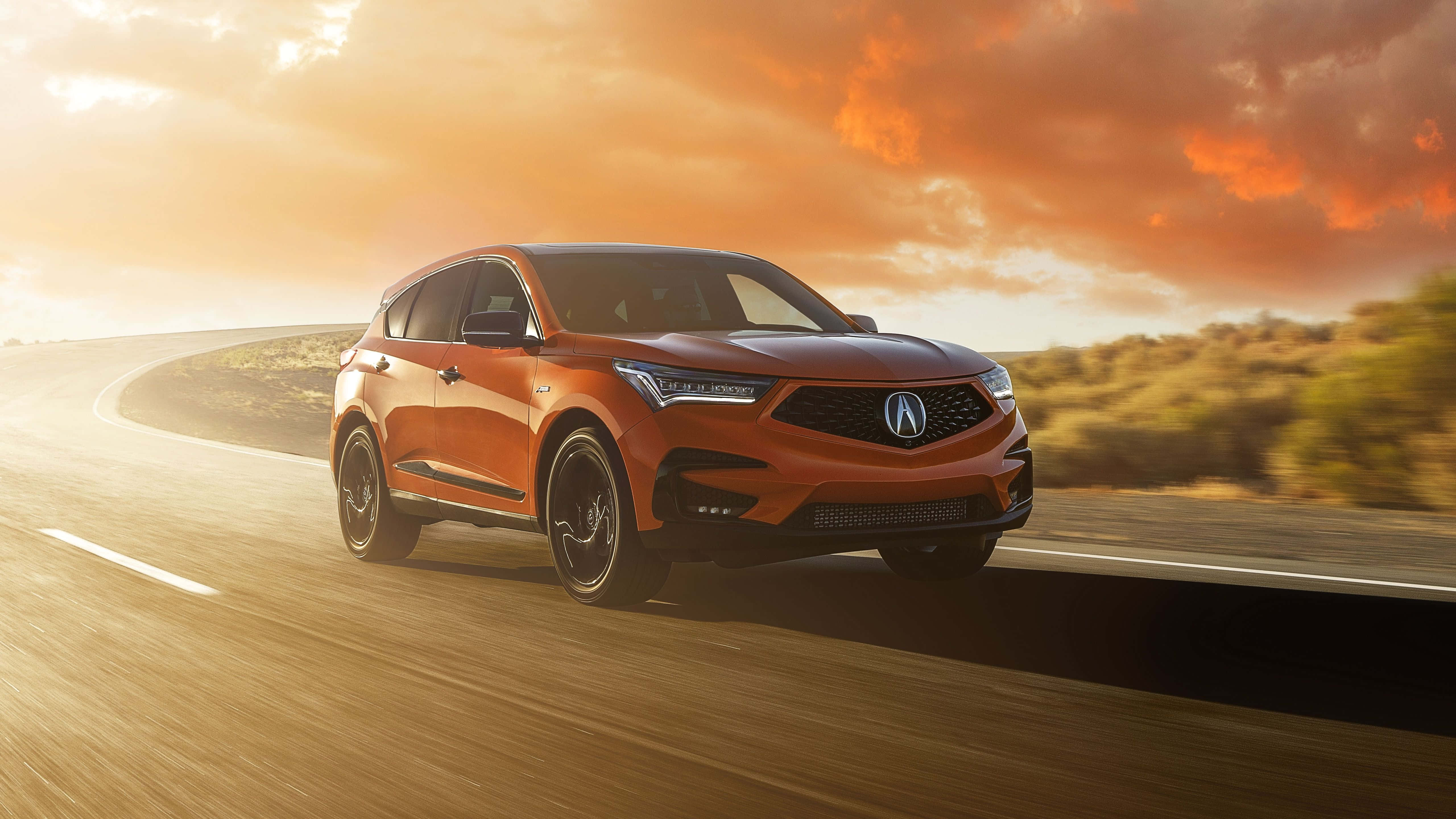 Acura Rdx 桌布 壁紙 — 一輛充滿活力的橙色Acura SUV在火燒般的日落天空下沿著蜿蜒的道路疾馳。