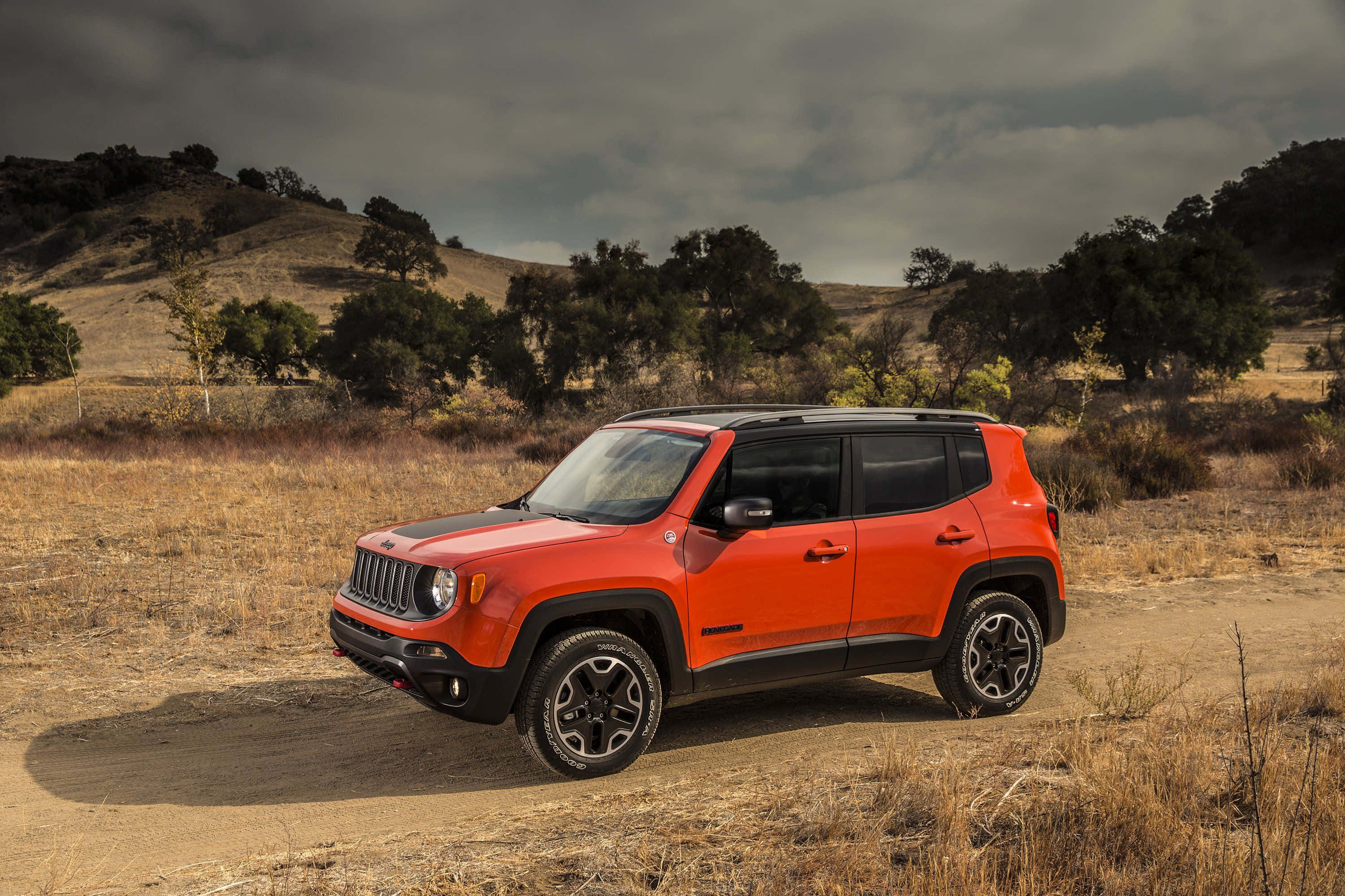 Jeep Renegade 桌布 壁紙 — 一輛充滿活力的橙色Jeep Renegade在乾燥草原的塵土小徑上，在陰沉的陰天天空下蓄勢待發。