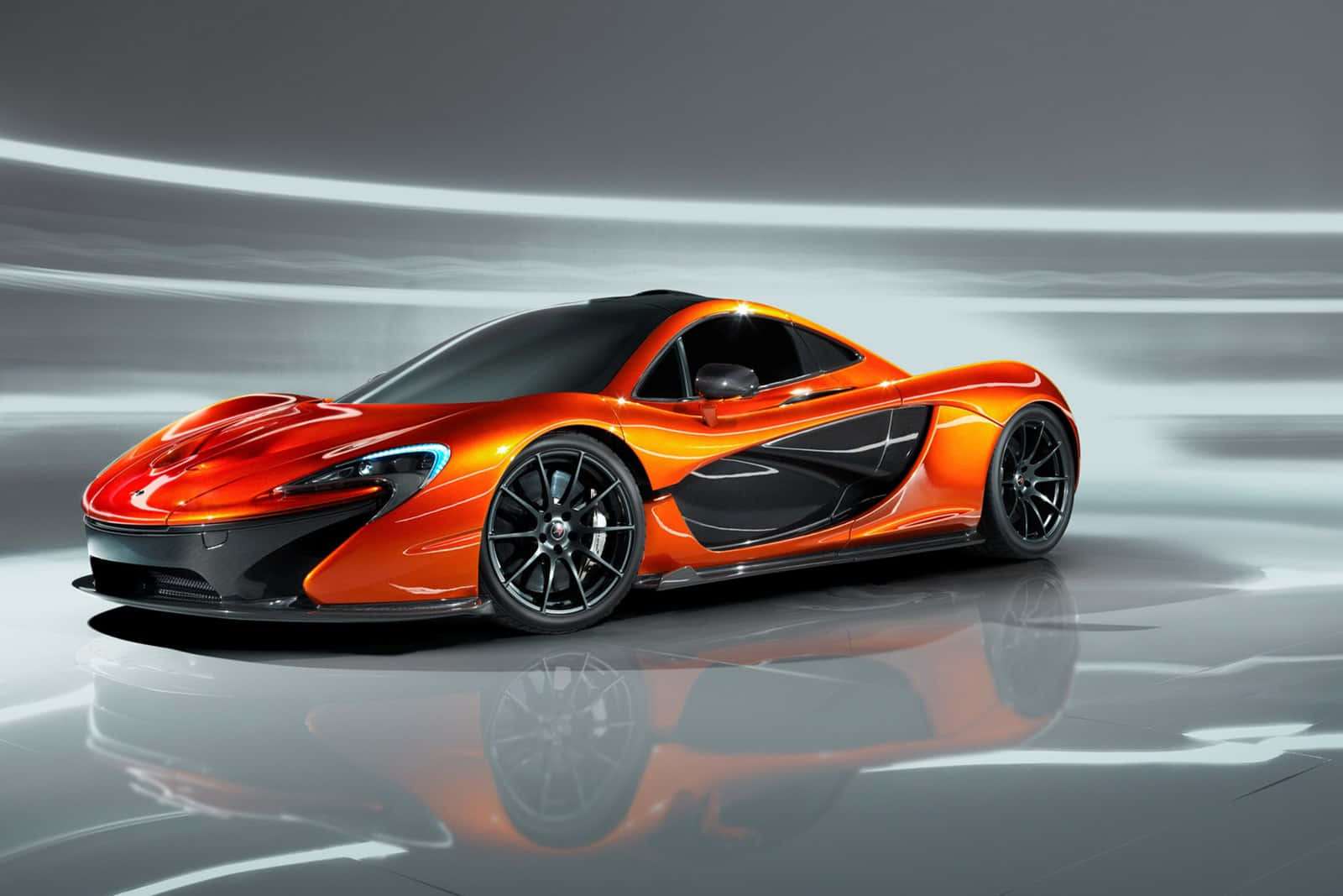 cars 桌布 壁紙 — 一輛充滿活力的橙色McLaren P1超級跑車在攝影棚燈光下，在反光地板上閃閃發光，背景帶有動態模糊條紋。