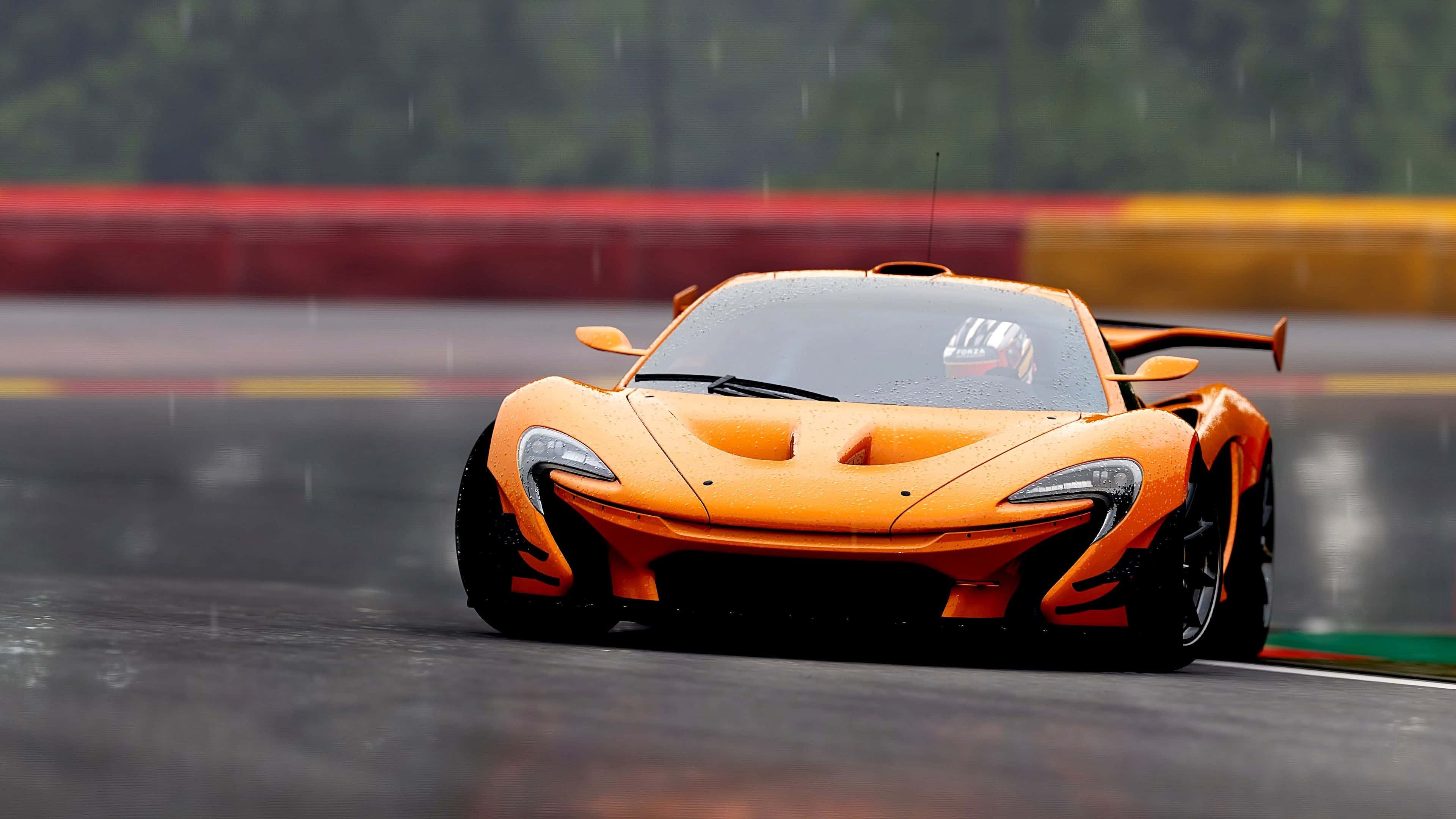 麥拿侖 桌布 壁紙 — 一輛充滿活力的橙色McLaren P1在潮濕的賽道上奔馳，雨滴在其流線型的空氣動力學車身上閃閃發光。