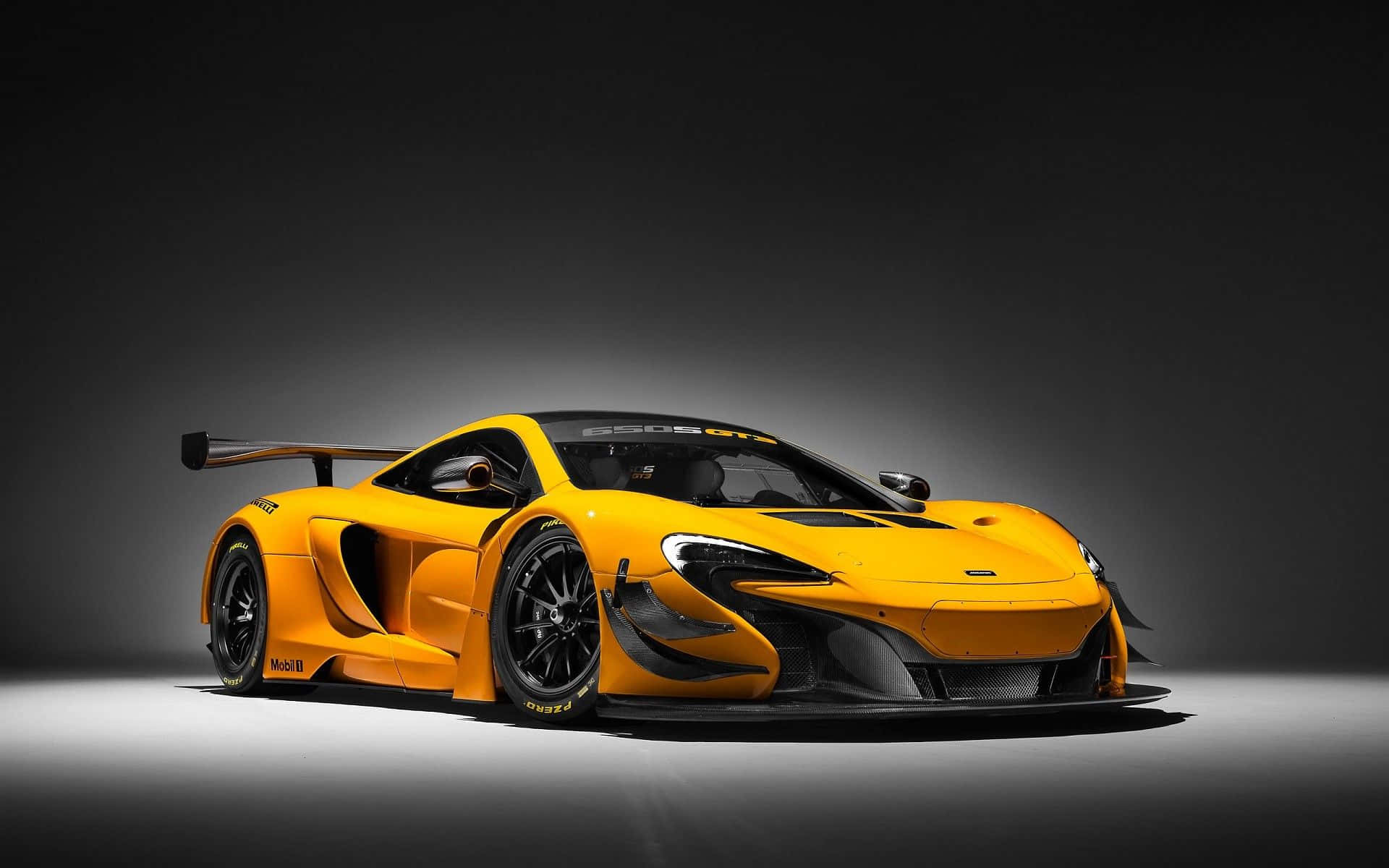 Yellow Car 桌布 壁紙 — 一輛充滿活力的橙色McLaren Senna GT賽車，帶有黑色飾邊和大型尾翼，在黑暗的攝影棚背景下戲劇性地打光。