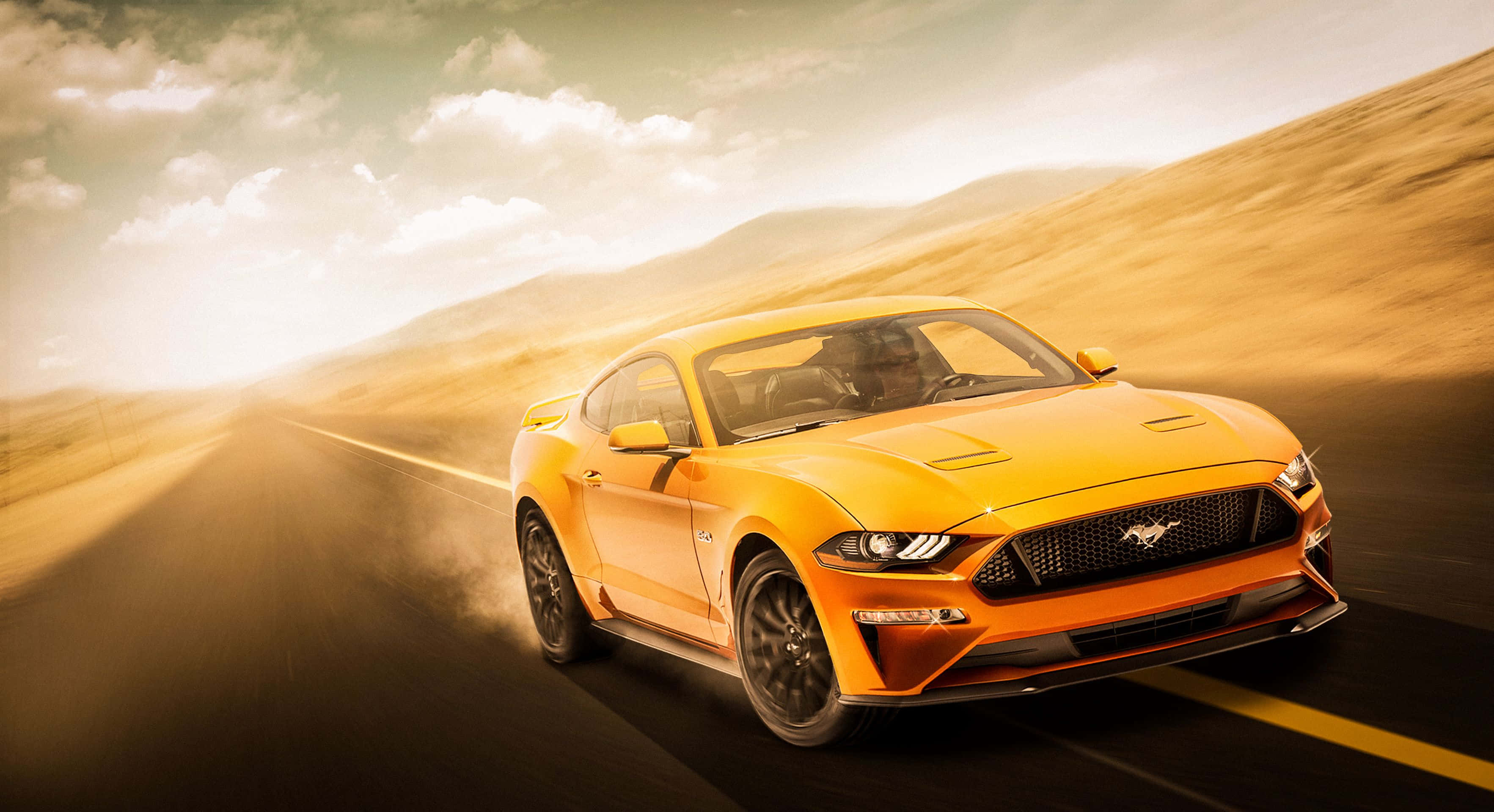 Yellow Car 桌布 壁紙 — 一輛充滿活力的橙色Mustang在金色日落天空下，以模糊的動感在沙漠公路上飛馳。