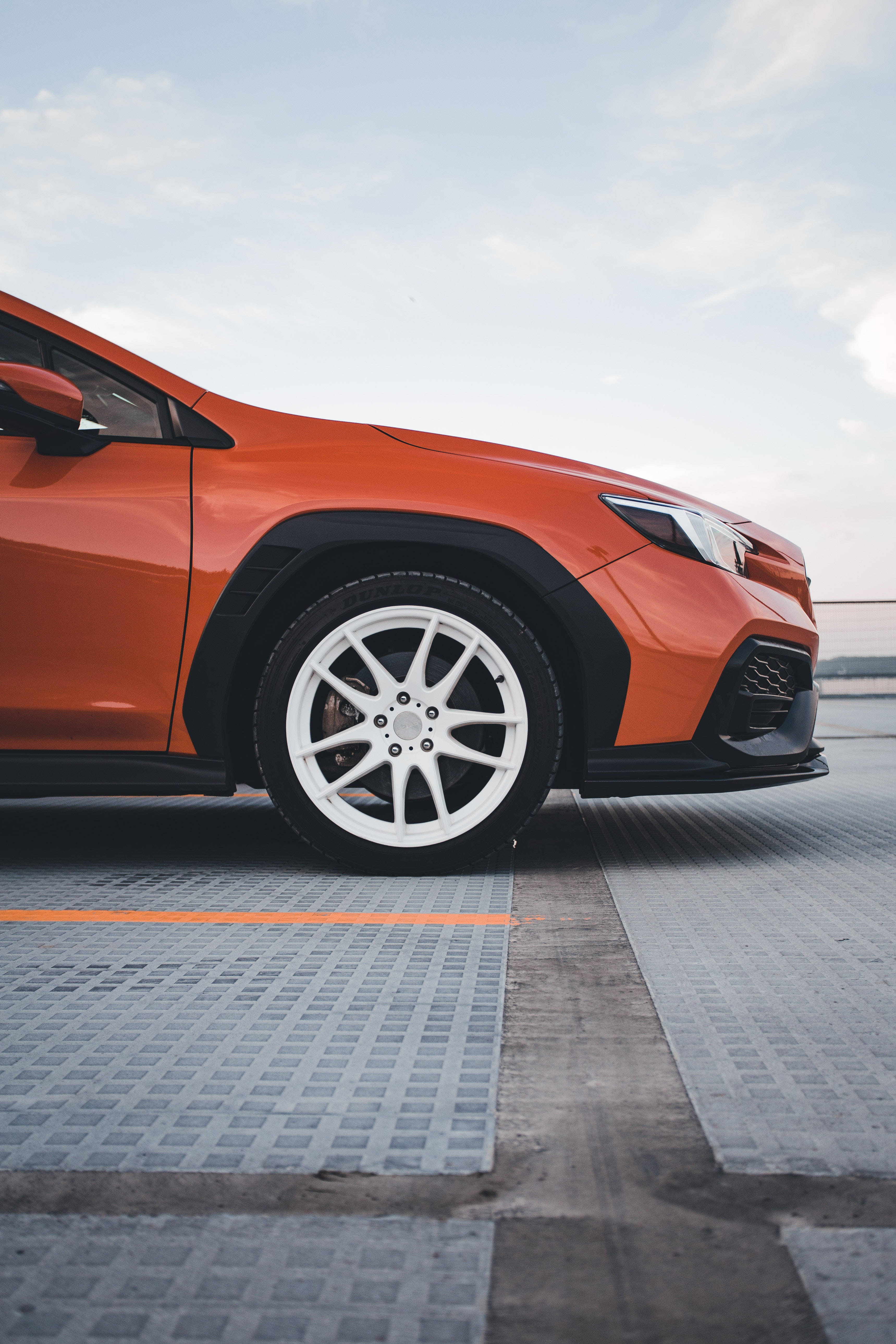 Sports Car 桌布 壁紙 — 一輛充滿活力的橙色SUV，白色車輪，停在紋理路面上，天空柔和。