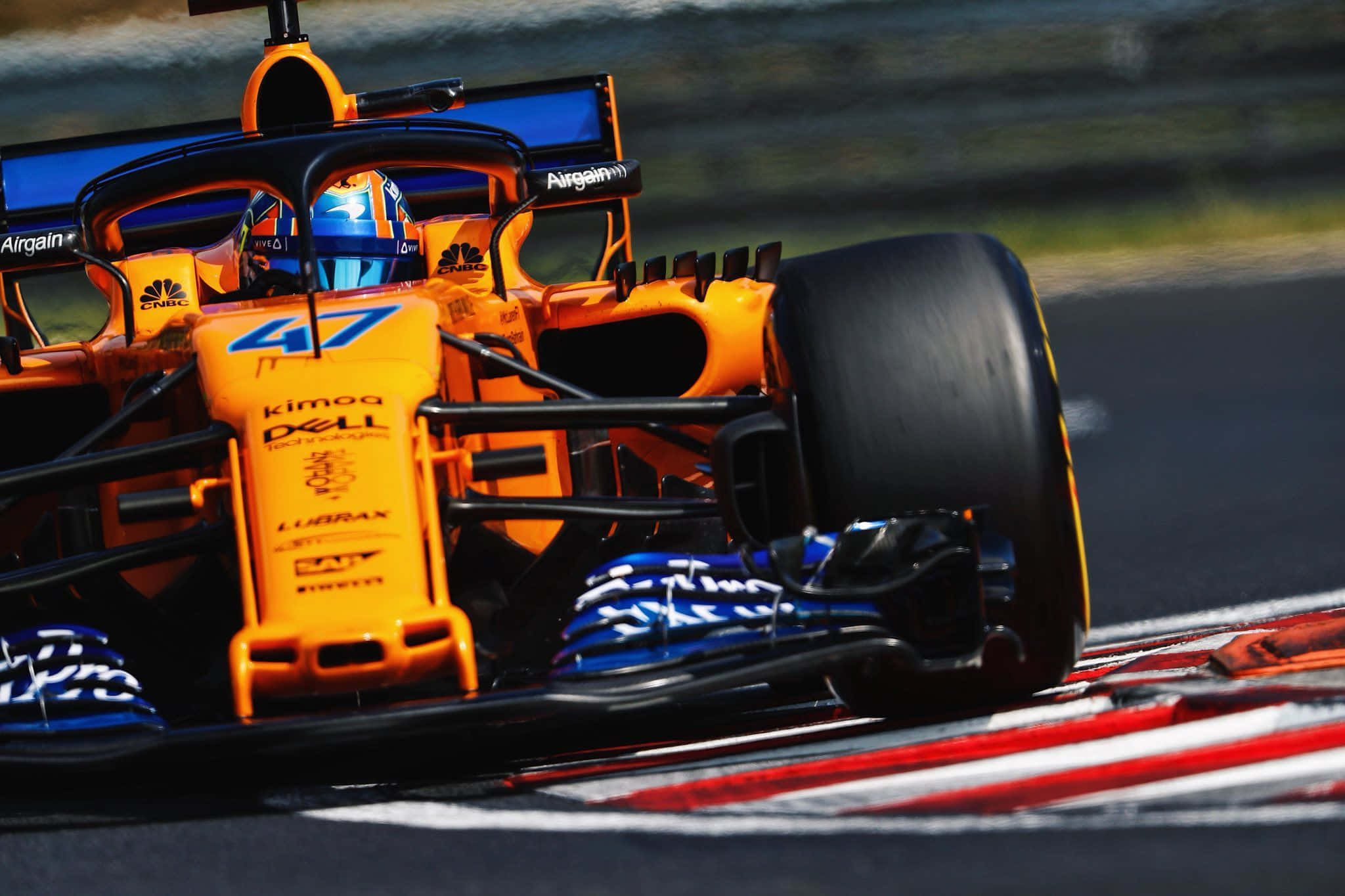 lando norris 桌布 壁紙 — 一輛充滿活力的橙色一級方程式賽車（編號47）在賽道上疾馳，帶有動態模糊效果和紅白路肩。