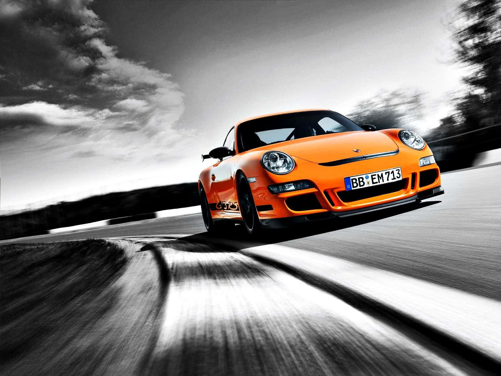 Car Design 桌布 壁紙 — 一輛充滿活力的橙色保時捷911 GT2在戲劇性的單色天空下，沿著模糊的瀝青賽道飛馳。