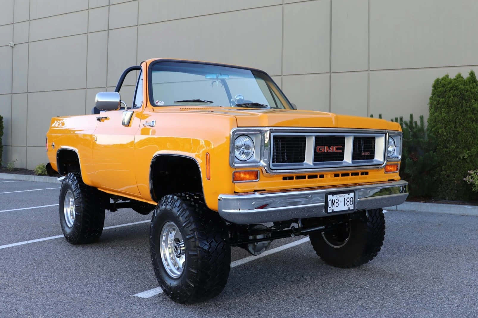Gmc Jimmy 桌布 壁紙 — 一輛充滿活力的橙色升高GMC皮卡車，帶有鍍鉻裝飾和大輪胎，停在現代化的停車場中。