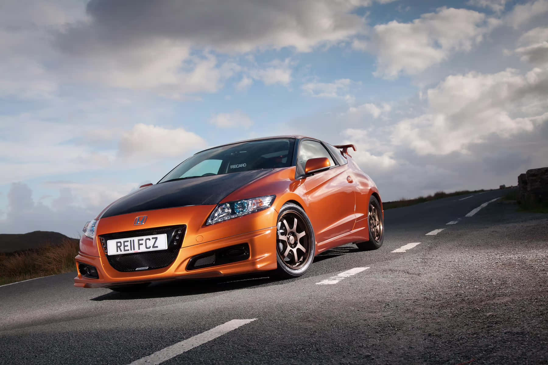 Honda Cr-z 桌布 壁紙 — 一輛充滿活力的橙色和黑色本田CR-Z跑車，帶有後擾流板，在陰天下行駛在蜿蜒的山路上。