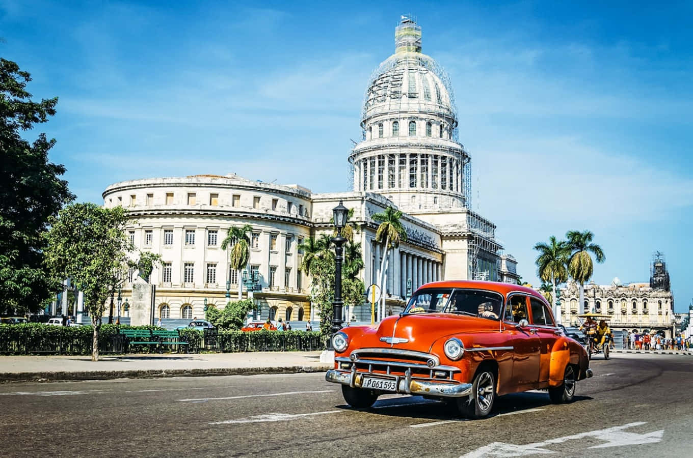 Cuba 桌布 壁紙 — 一輛充滿活力的橙色復古車在哈瓦那晴朗的藍天下駛過宏偉的國會大廈。