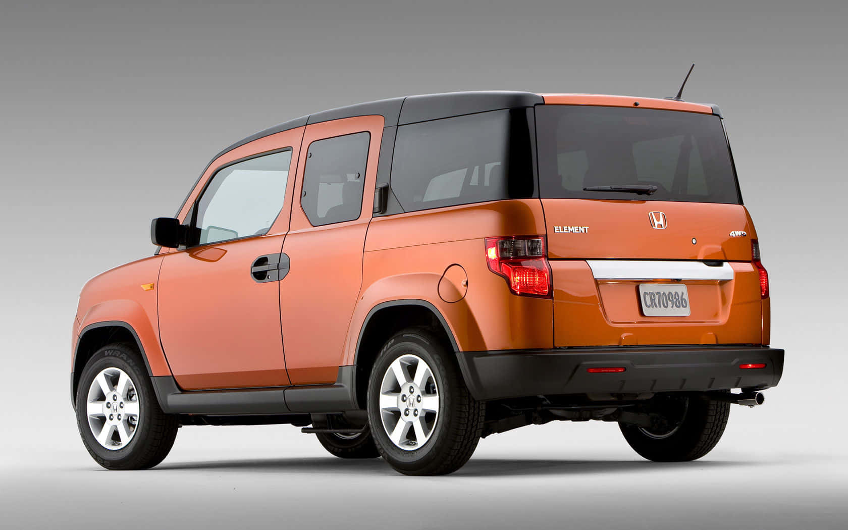 Honda Element 桌布 壁紙 — 一輛充滿活力的橙色本田 Element SUV，從後方四分之三角度拍攝，背景為中性灰色工作室背景。