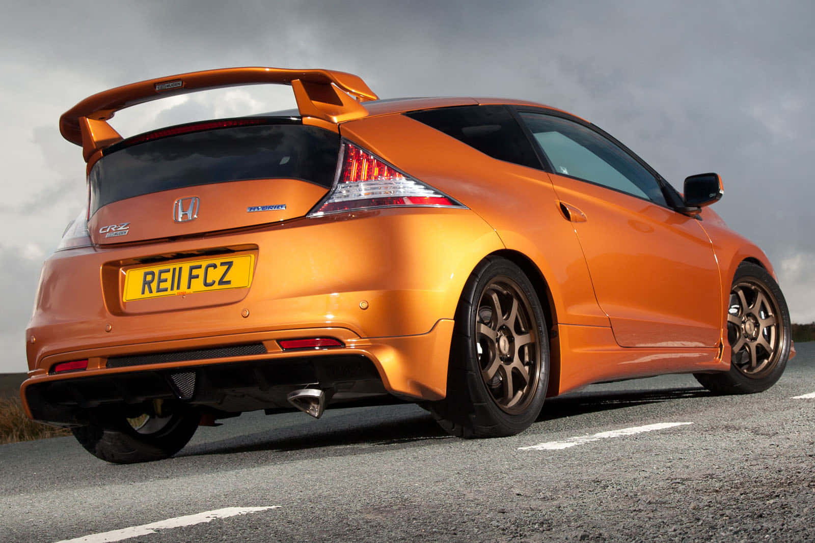 Honda Cr-z 桌布 壁紙 — 一輛充滿活力的橙色本田CR-Z跑車，帶有大型後擾流板，停在陰天下的瀝青路上。
