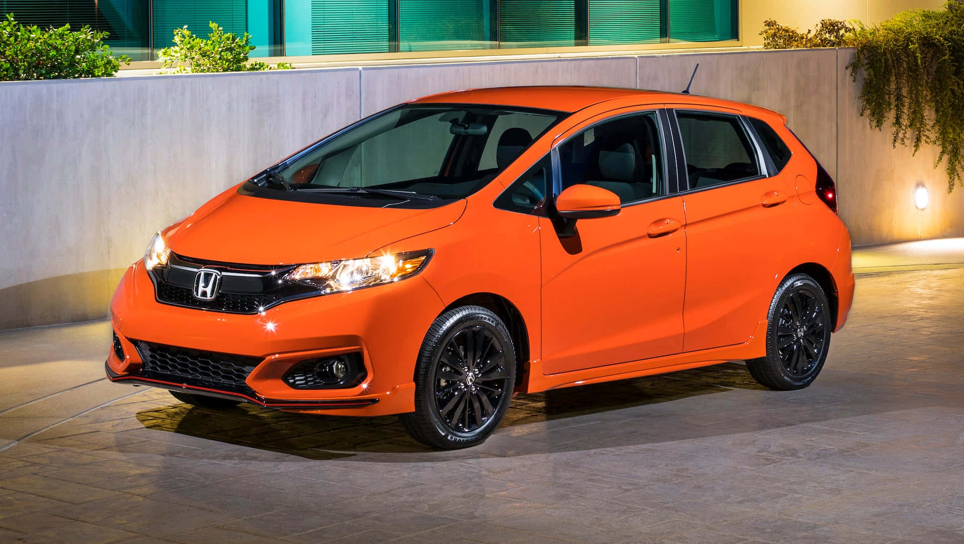 Honda Fit 桌布 壁紙 — 一輛充滿活力的橙色本田Fit在夜間停車，車頭燈發光，黑色輪圈，背景是現代混凝土牆。