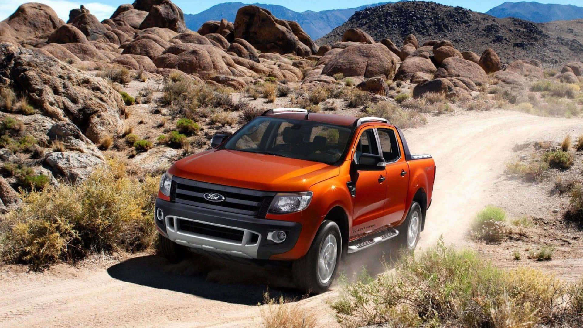 Ford Ranger 桌布 壁紙 — 一輛充滿活力的橙色福特皮卡車在晴朗的藍天下，沿著崎嶇的沙漠小徑行駛，揚起灰塵，周圍是岩石地形和稀疏的灌木叢。