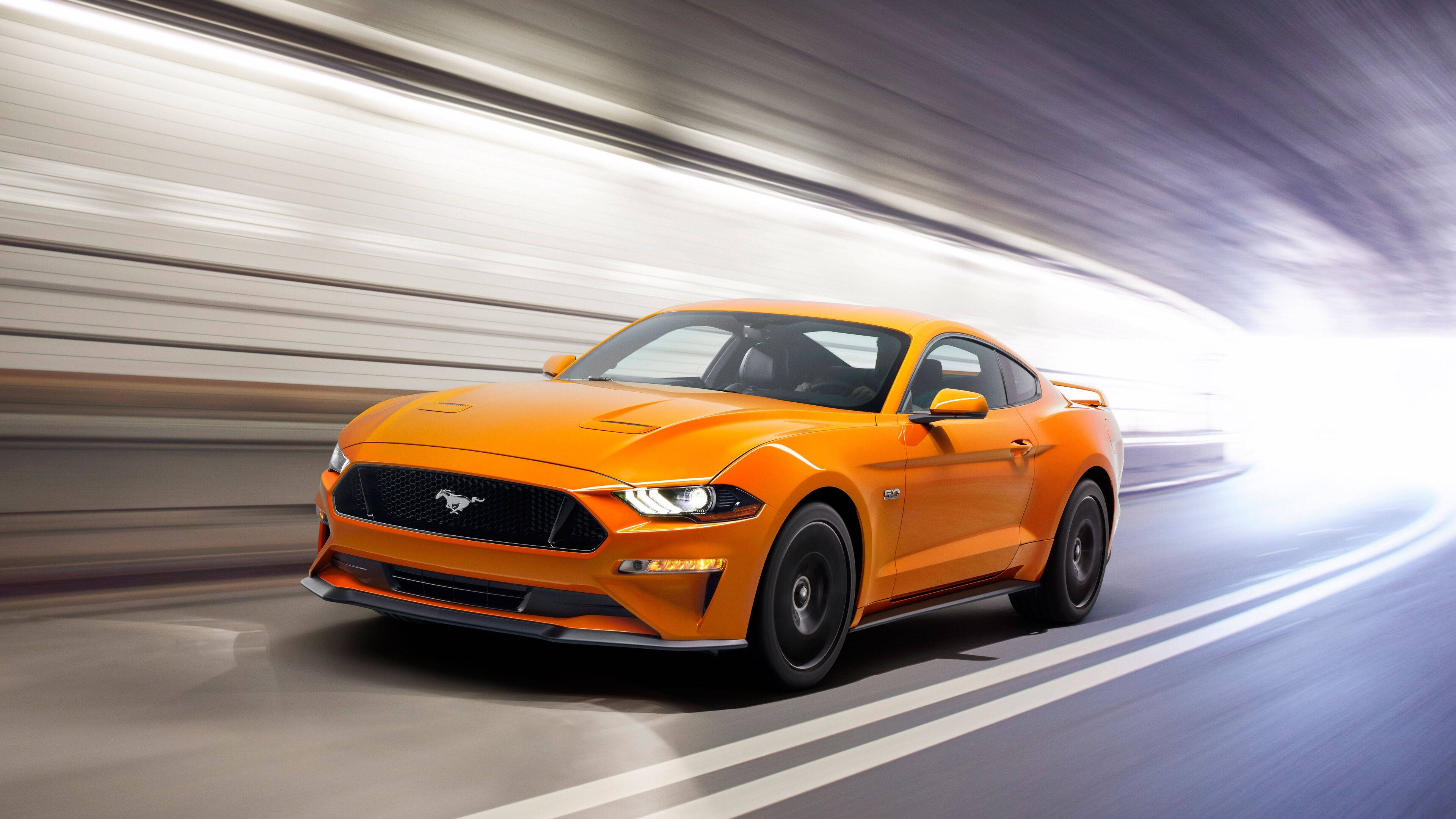 mustang HD 桌布 壁紙 — 一輛充滿活力的橙色福特野馬在模糊的高速公路上疾馳，運動線條強調其高速。