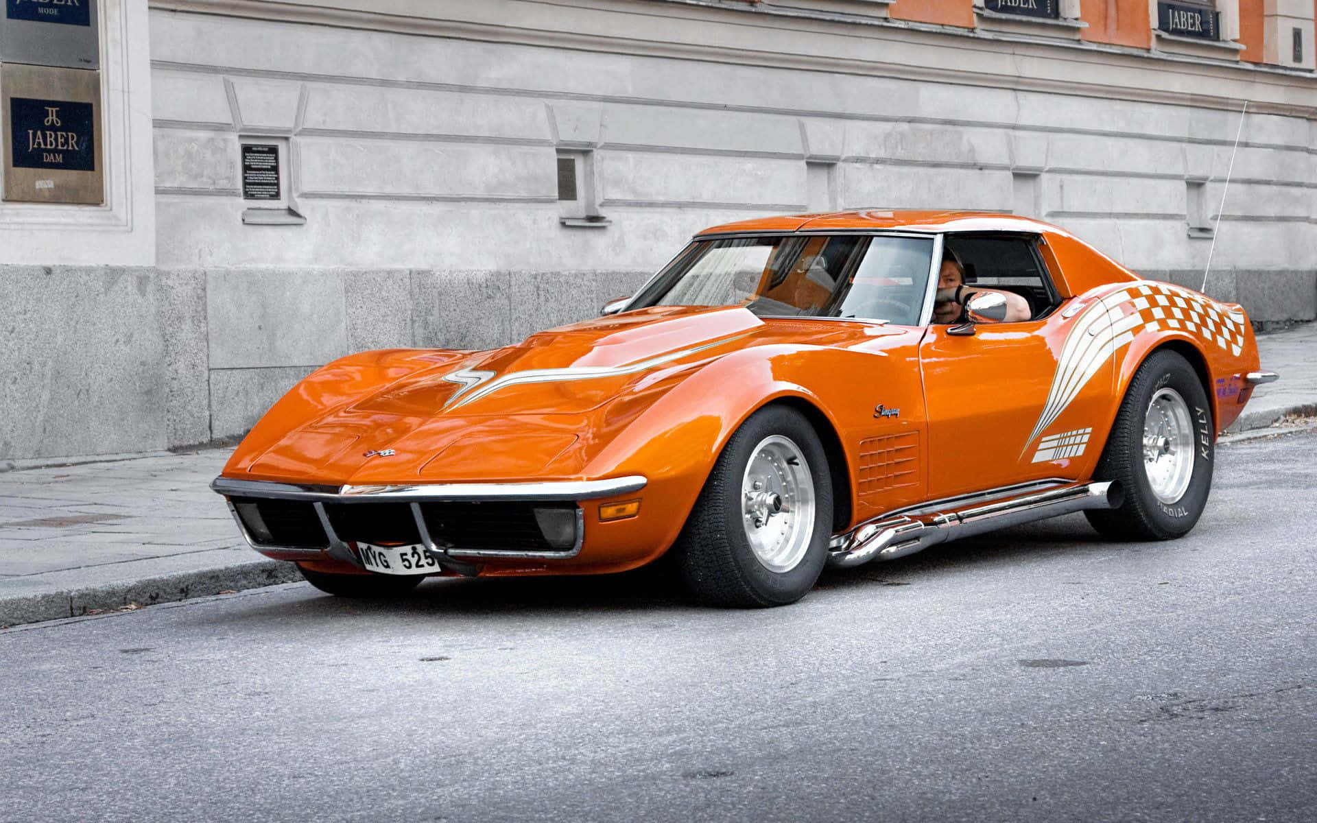 classic 桌布 壁紙 — 一輛充滿活力的橙色經典Corvette跑車，帶有格子側面貼花，停放在城市街道上。