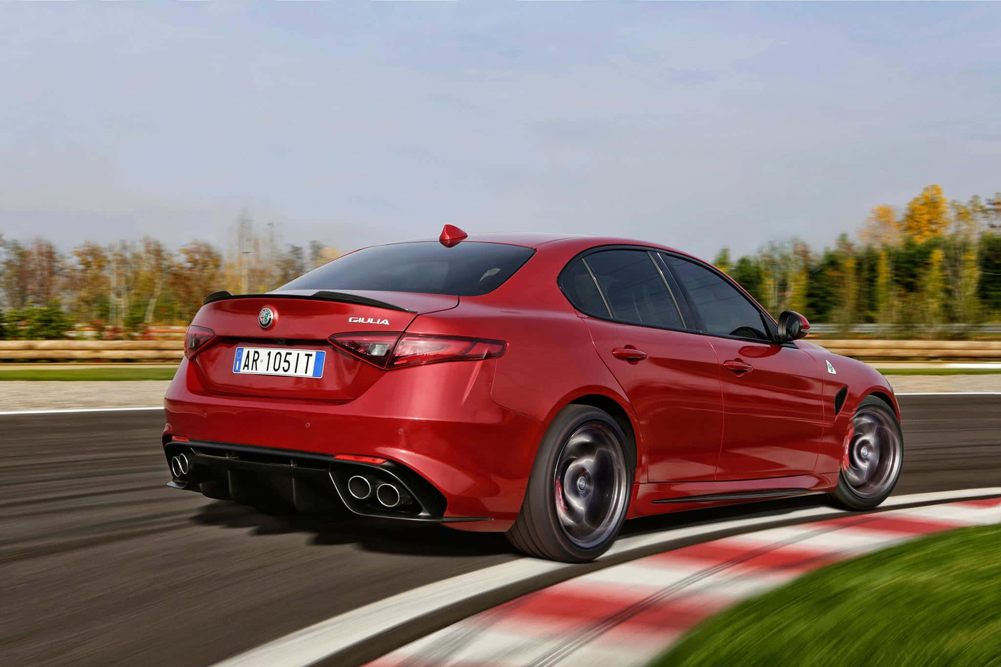 Alfa Romeo Giulia 桌布 壁紙 — 一輛充滿活力的紅色 Alfa Romeo Giulia 運動轎車在賽道彎道上高速行駛，背景是模糊的動態和秋樹。
