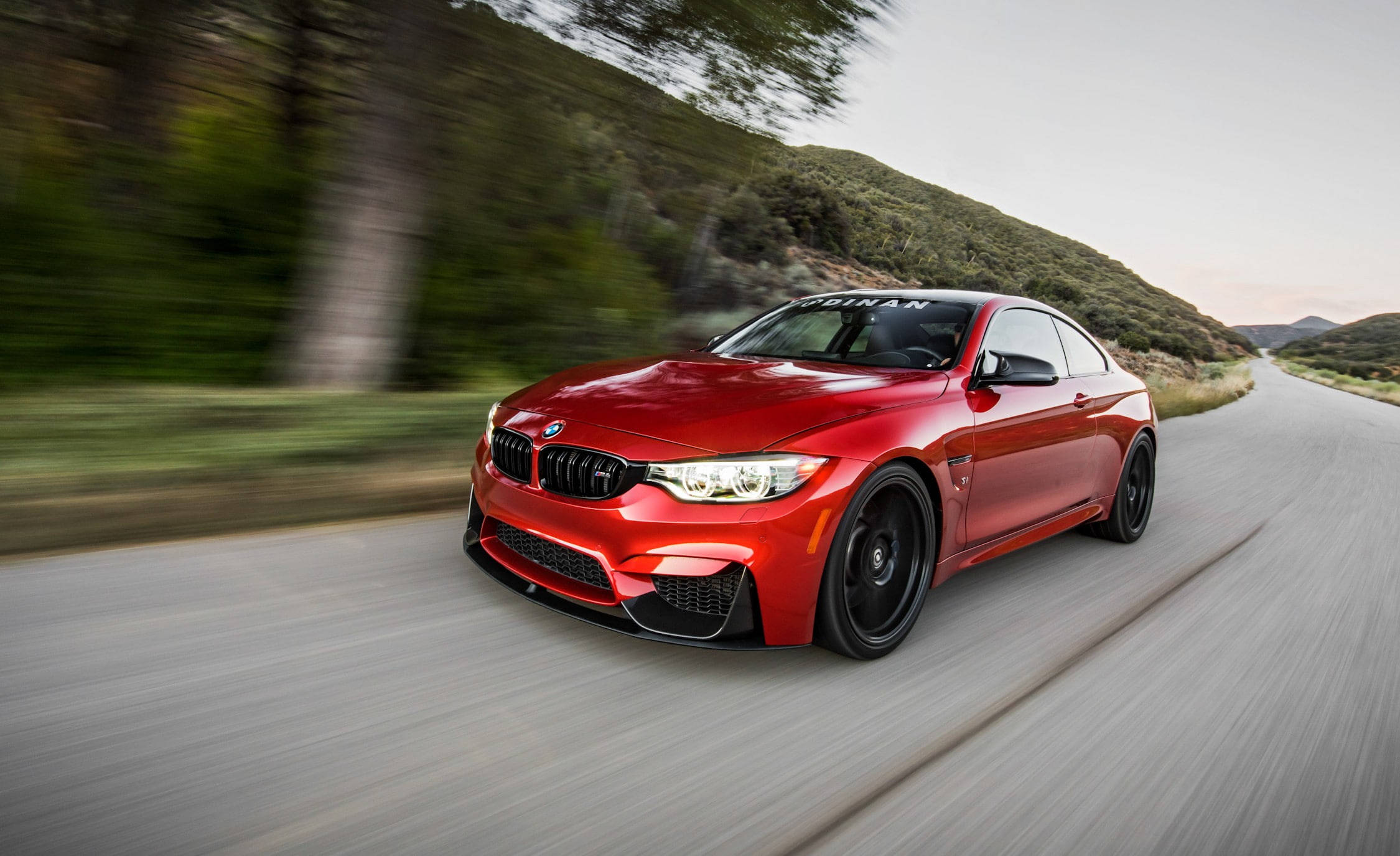Sports Car 桌布 壁紙 — 一輛充滿活力的紅色BMW M4雙門跑車沿著蜿蜒的山路疾馳，動態模糊強調了它的速度。