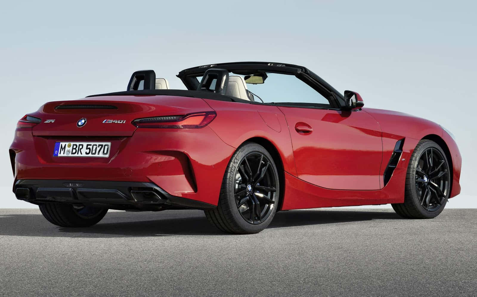 Bmw Z4 桌布 壁紙 — 一輛充滿活力的紅色BMW Z4開篷跑車，帶有黑色飾件和流線型設計，停泊在晴朗天空下的瀝青路面上。