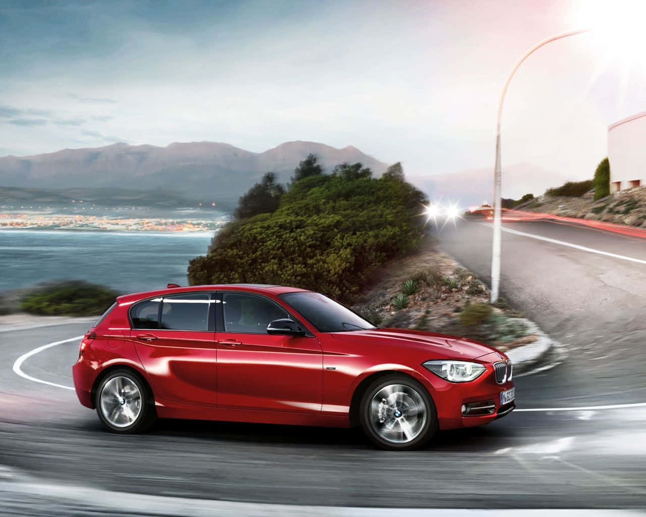 Bmw 1 Series 桌布 壁紙 — 一輛充滿活力的紅色BMW掀背車沿著海岸公路飛馳，背景是山脈和海洋。